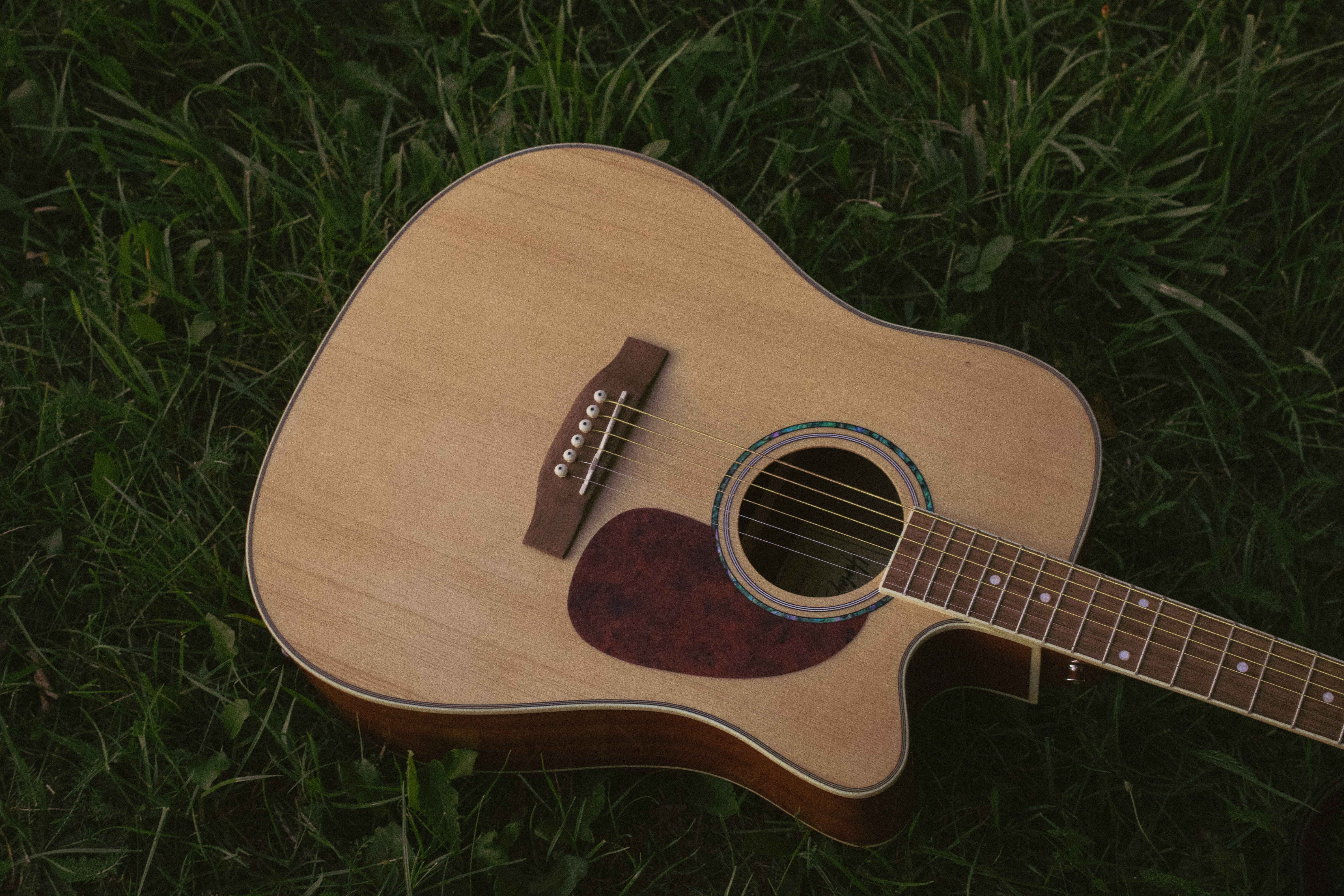 An acoustic guitar with a wooden body resting on green grass