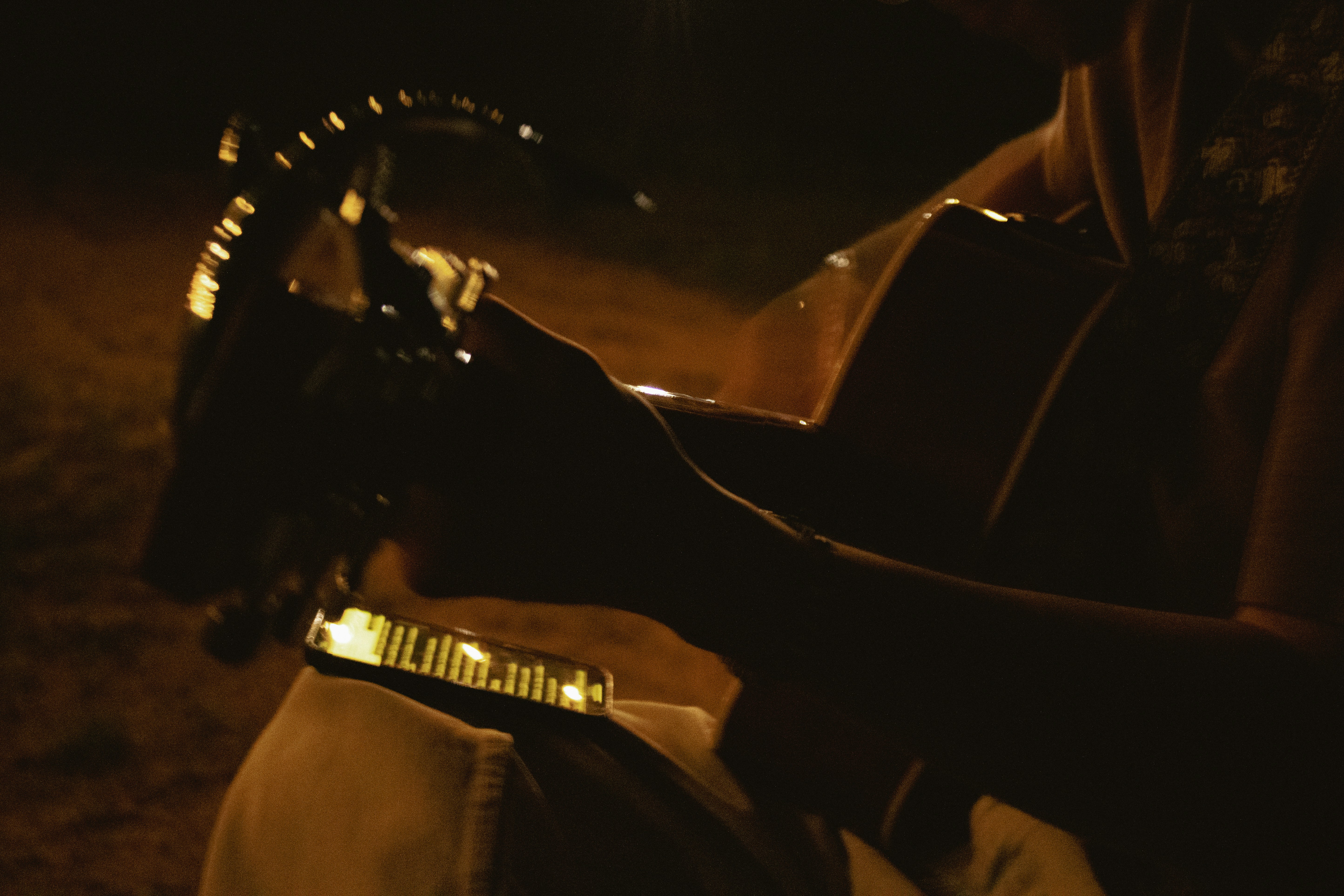 A person playing an acoustic guitar in dim warm light at night