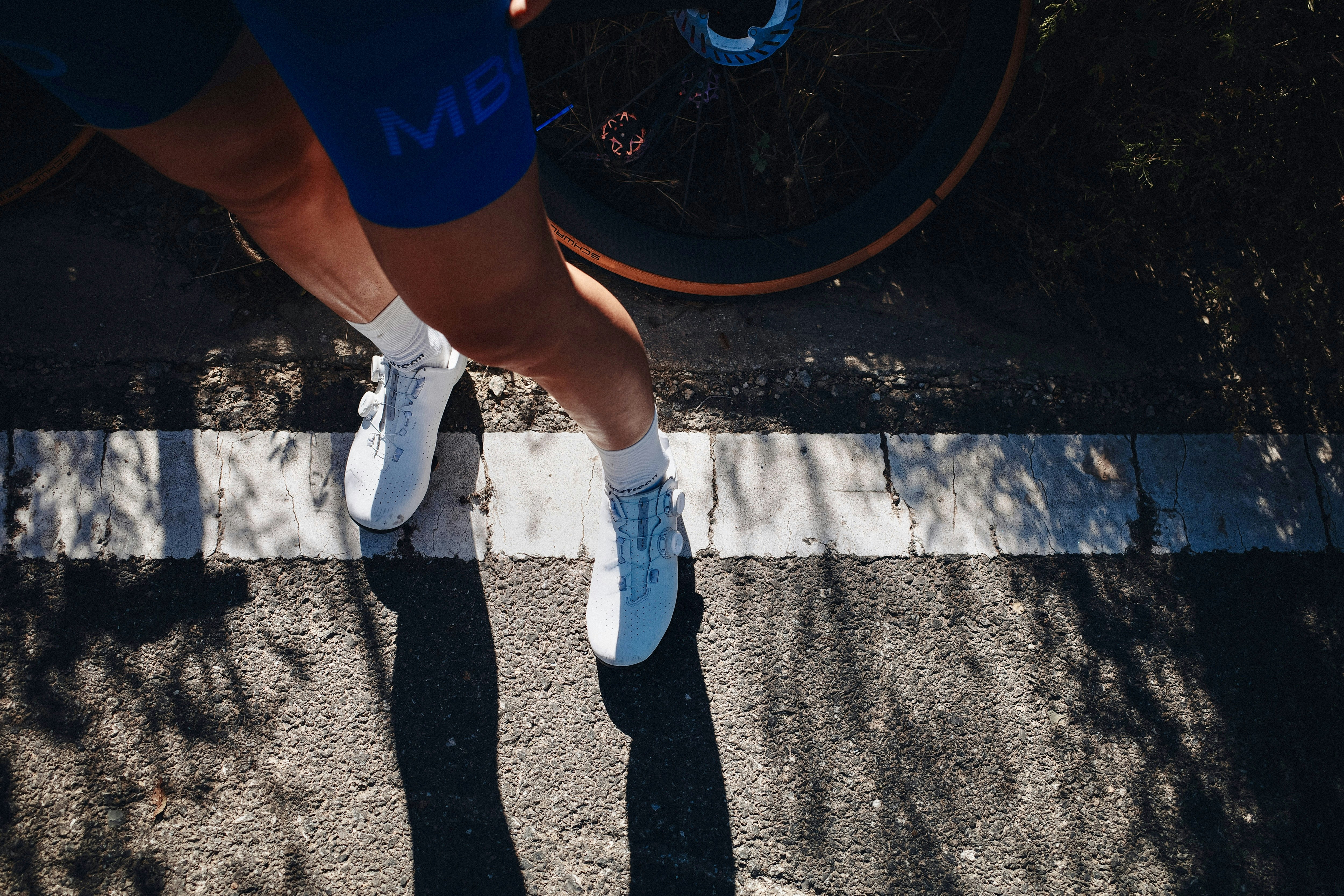 A cyclist wearing white shoes and blue shorts on a paved road