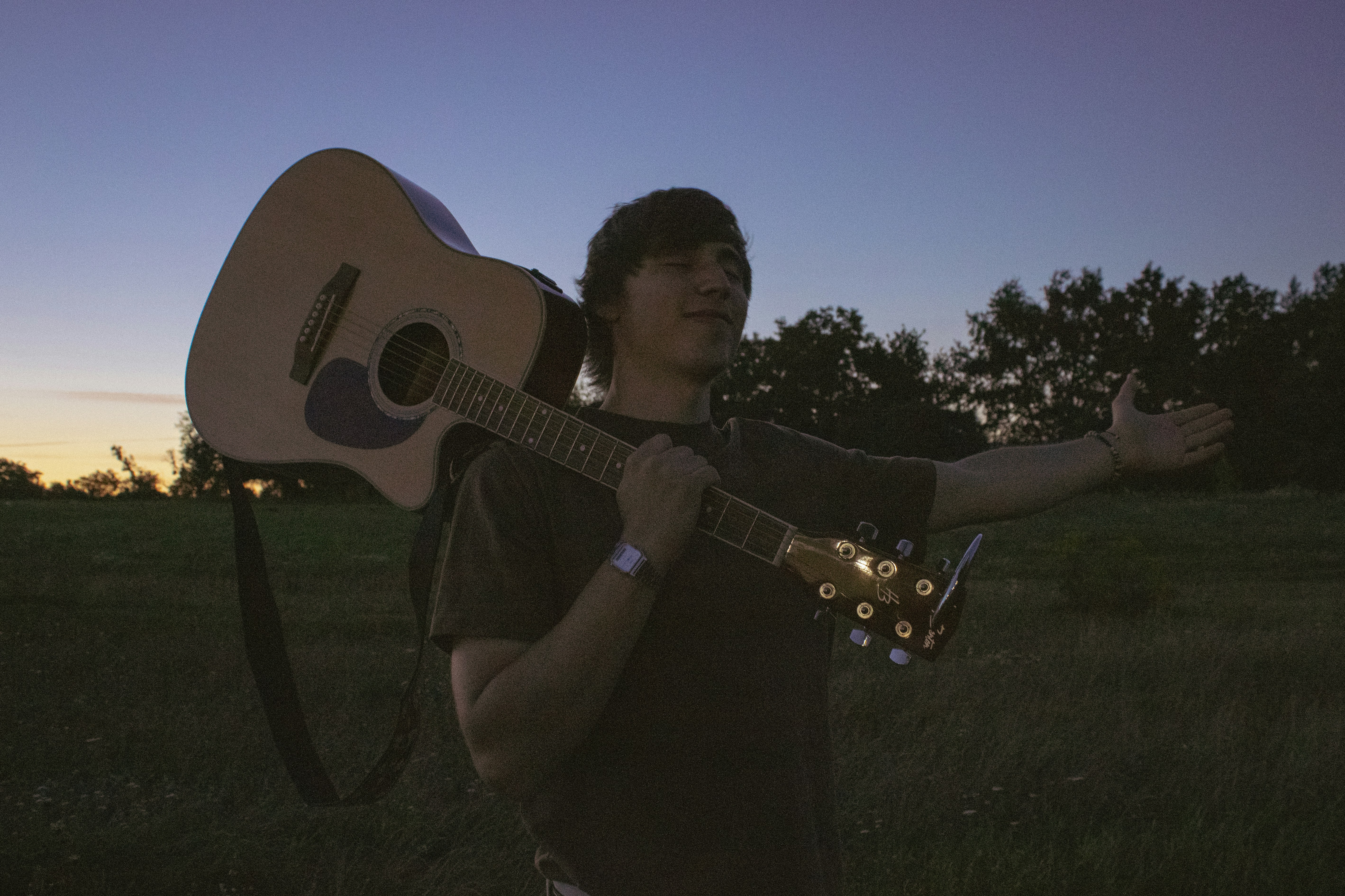 A person carrying an acoustic guitar on their shoulder in a grassy field