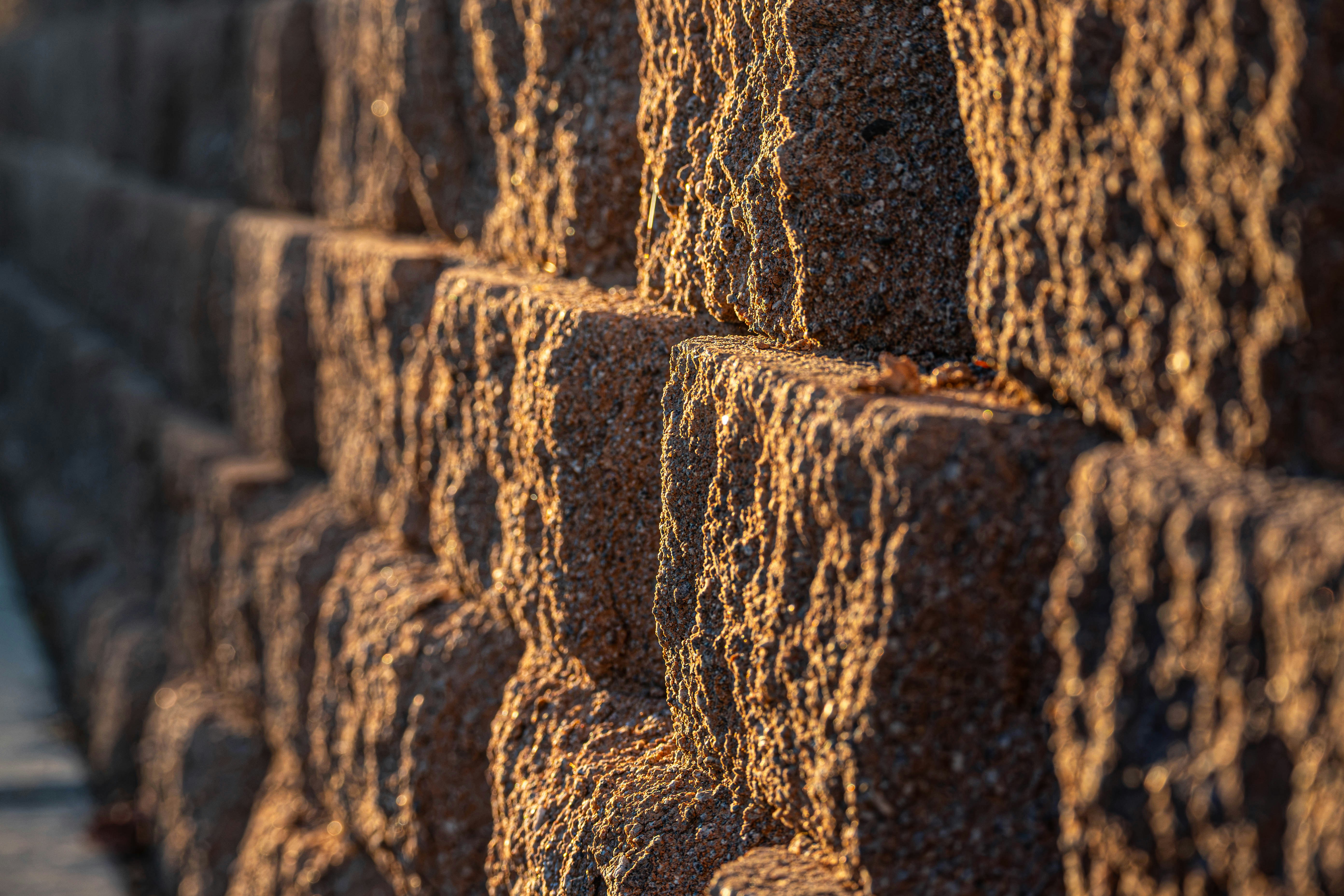 Close view of a segmental concrete block retaining wall, split face blocks stacked in a running bond with each course set back, lit by low sun