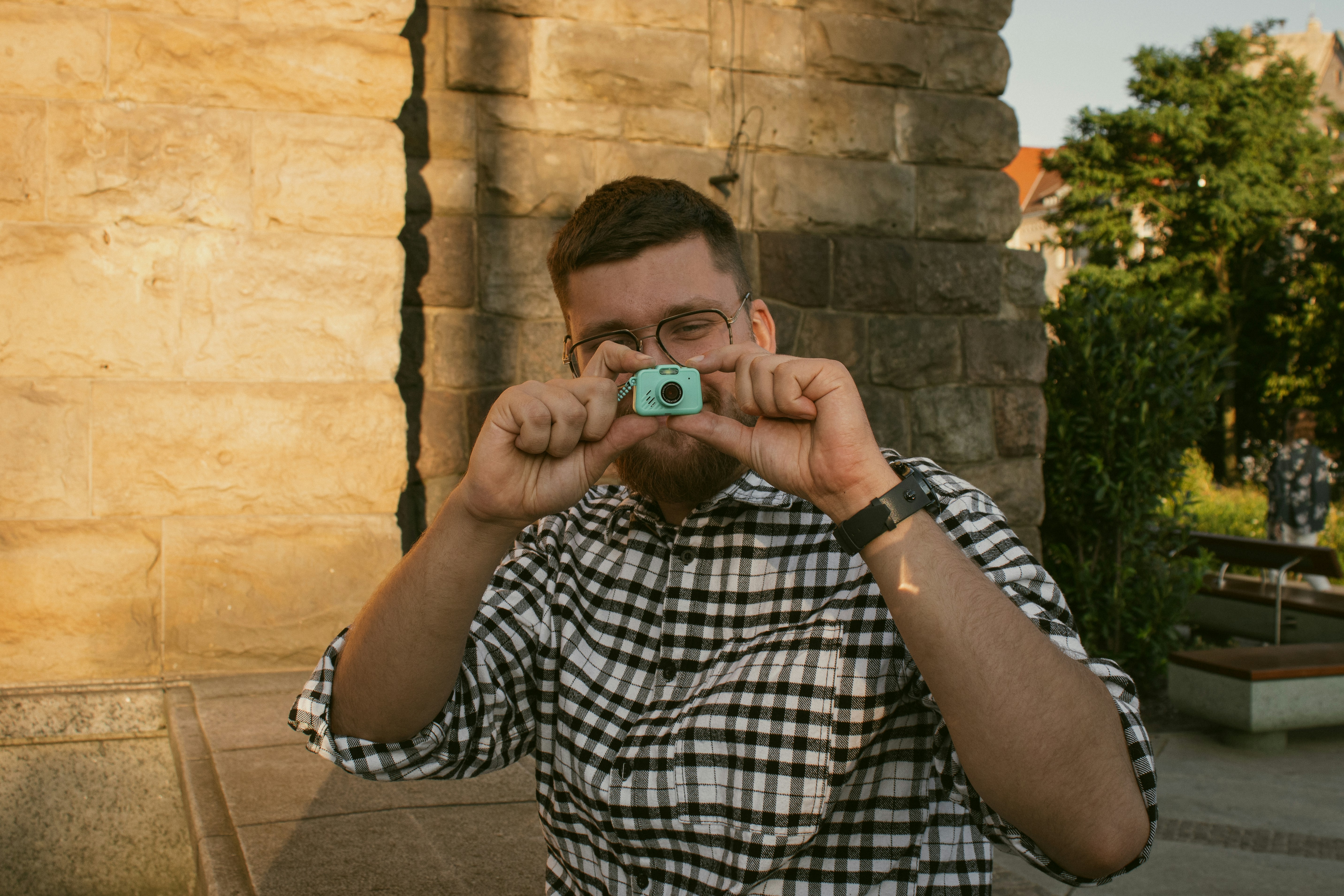 A man in a black and white plaid shirt holding a small toy camera