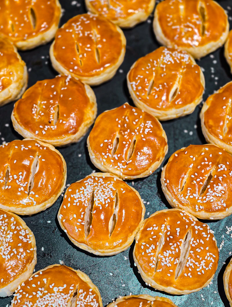 Golden wife cakes topped with sesame seeds on a baking tray