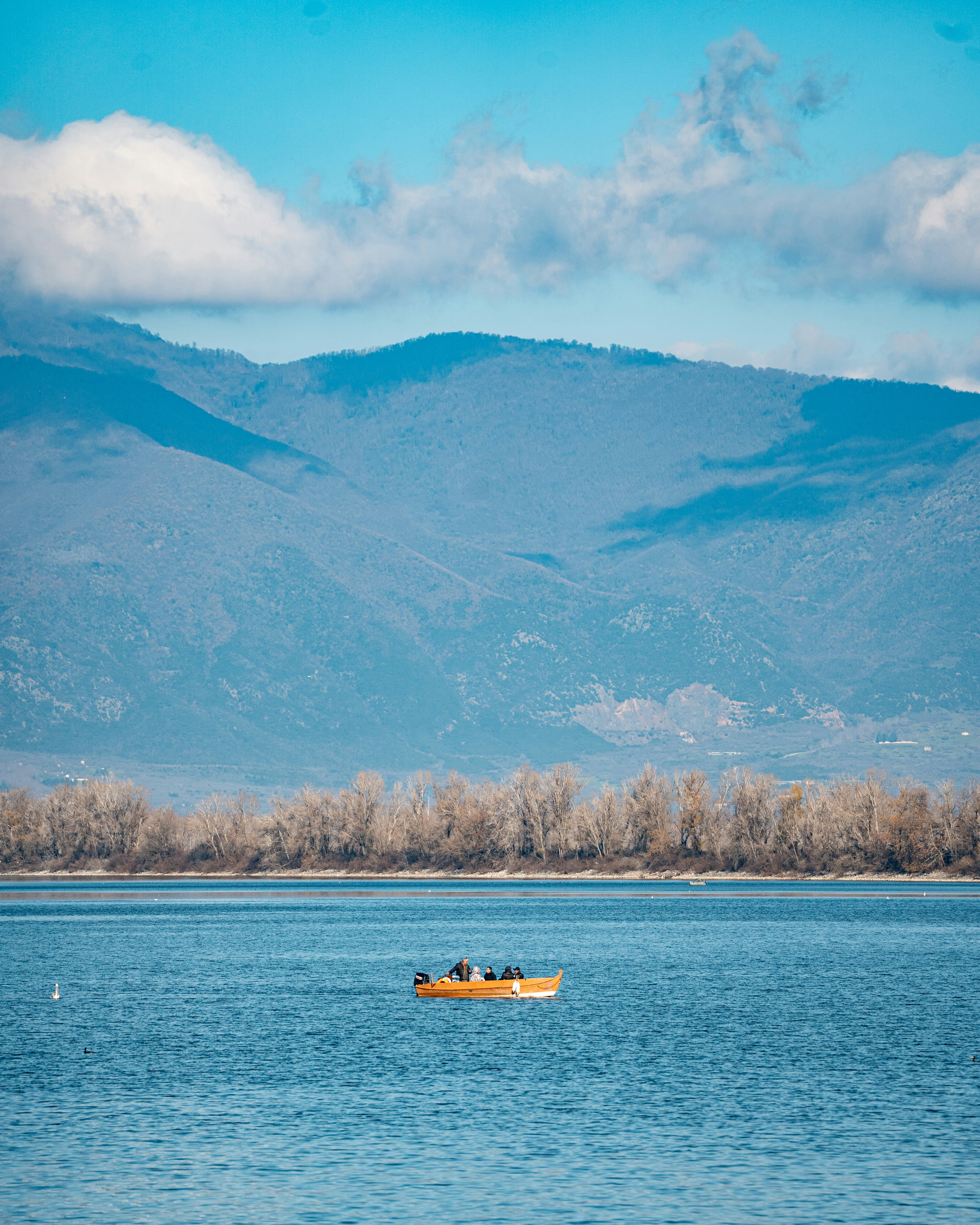 A small wooden boat with people on a calm lake before distant mountains