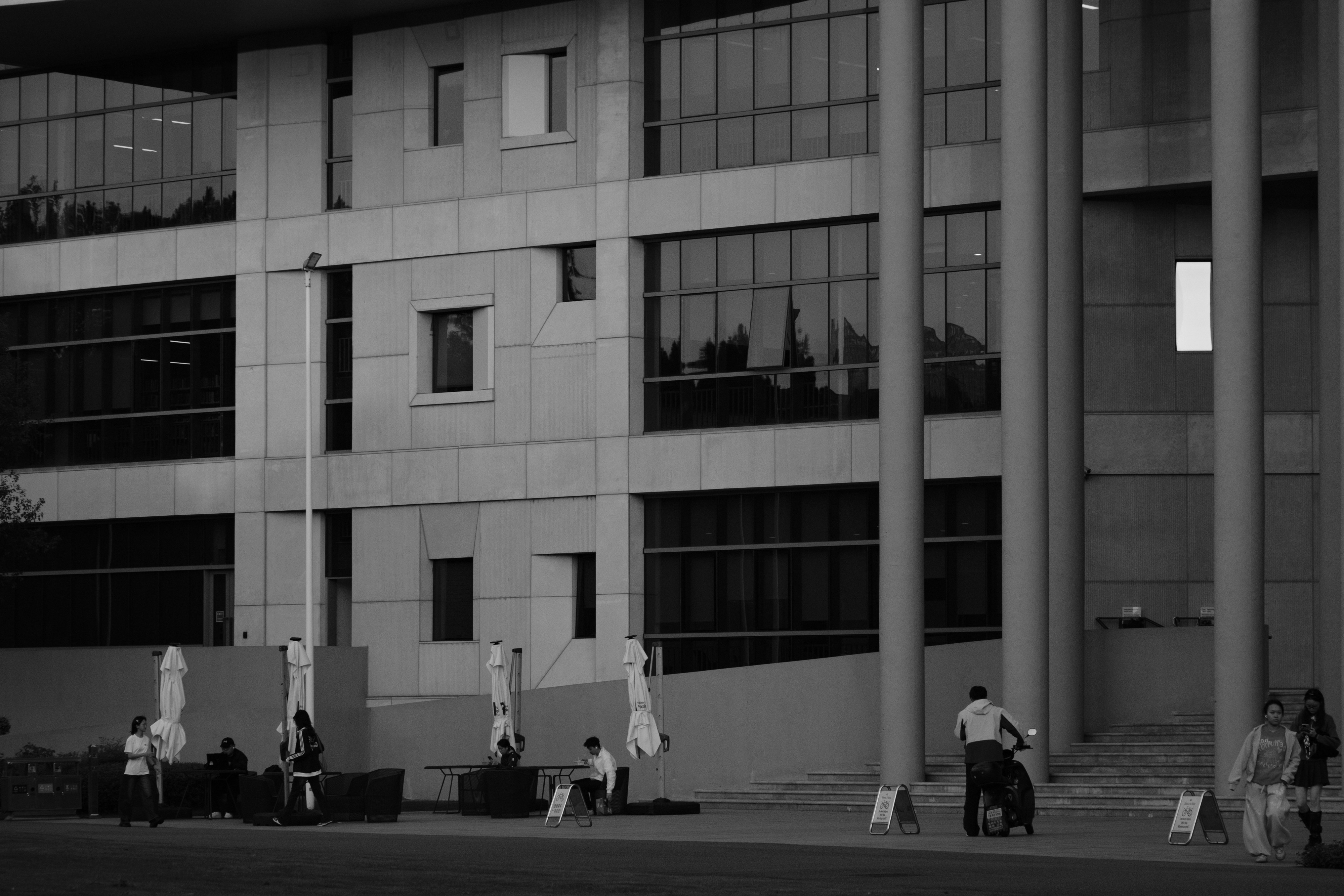 People walking and sitting near a modern building with large glass windows