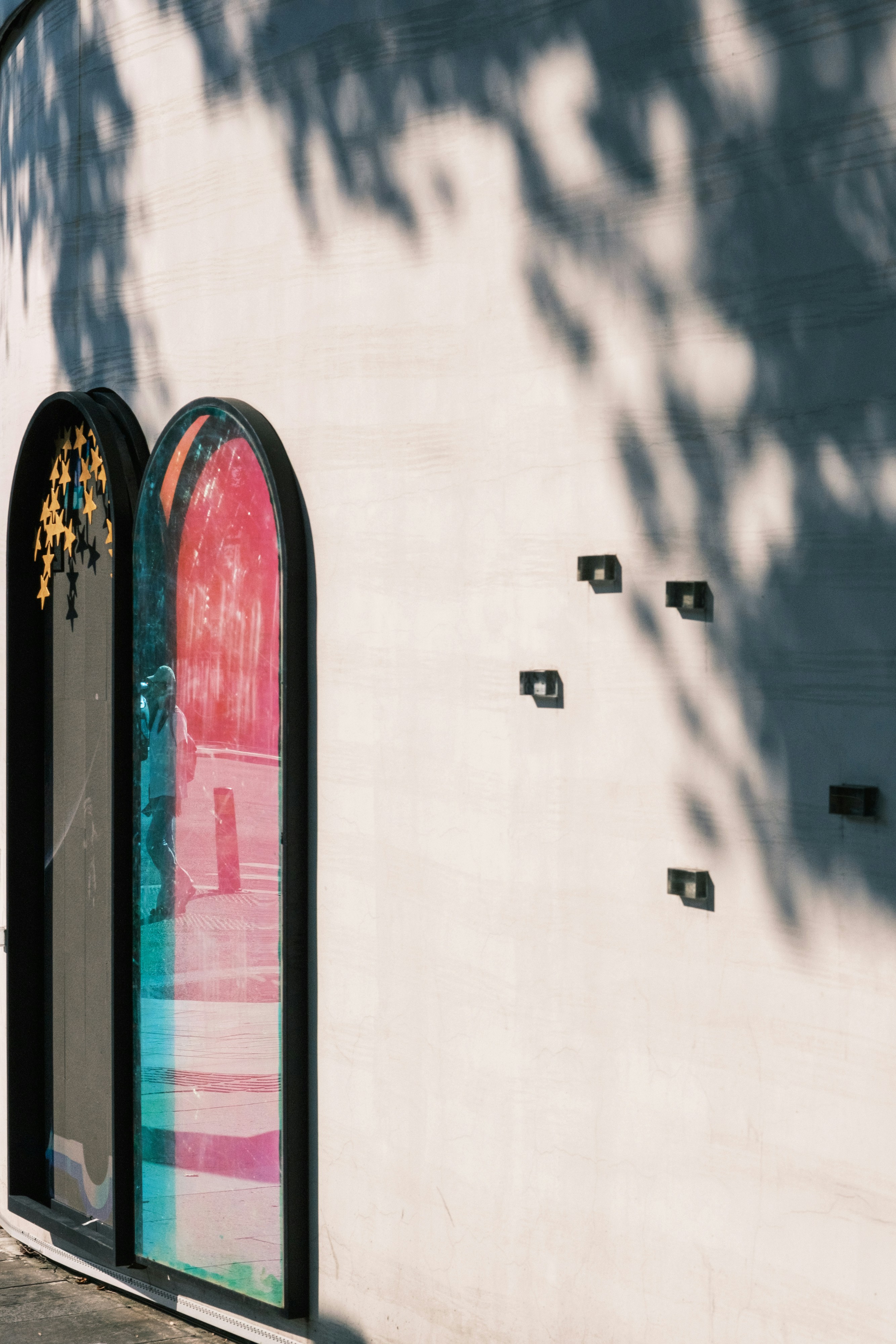 A person reflected in a colorful arched window on a white wall with shadows