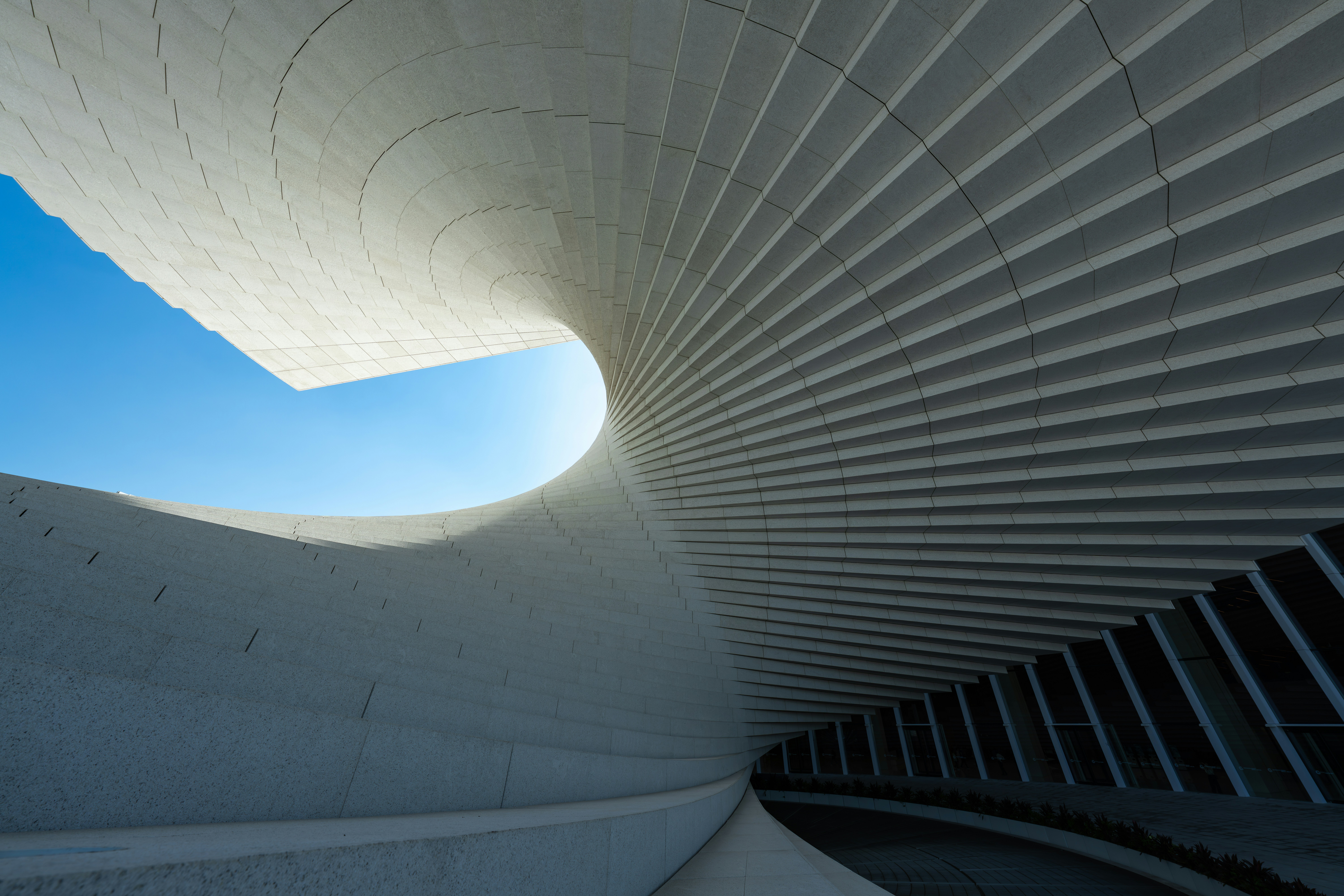 A curved white architectural structure with repeating panels against a clear blue sky