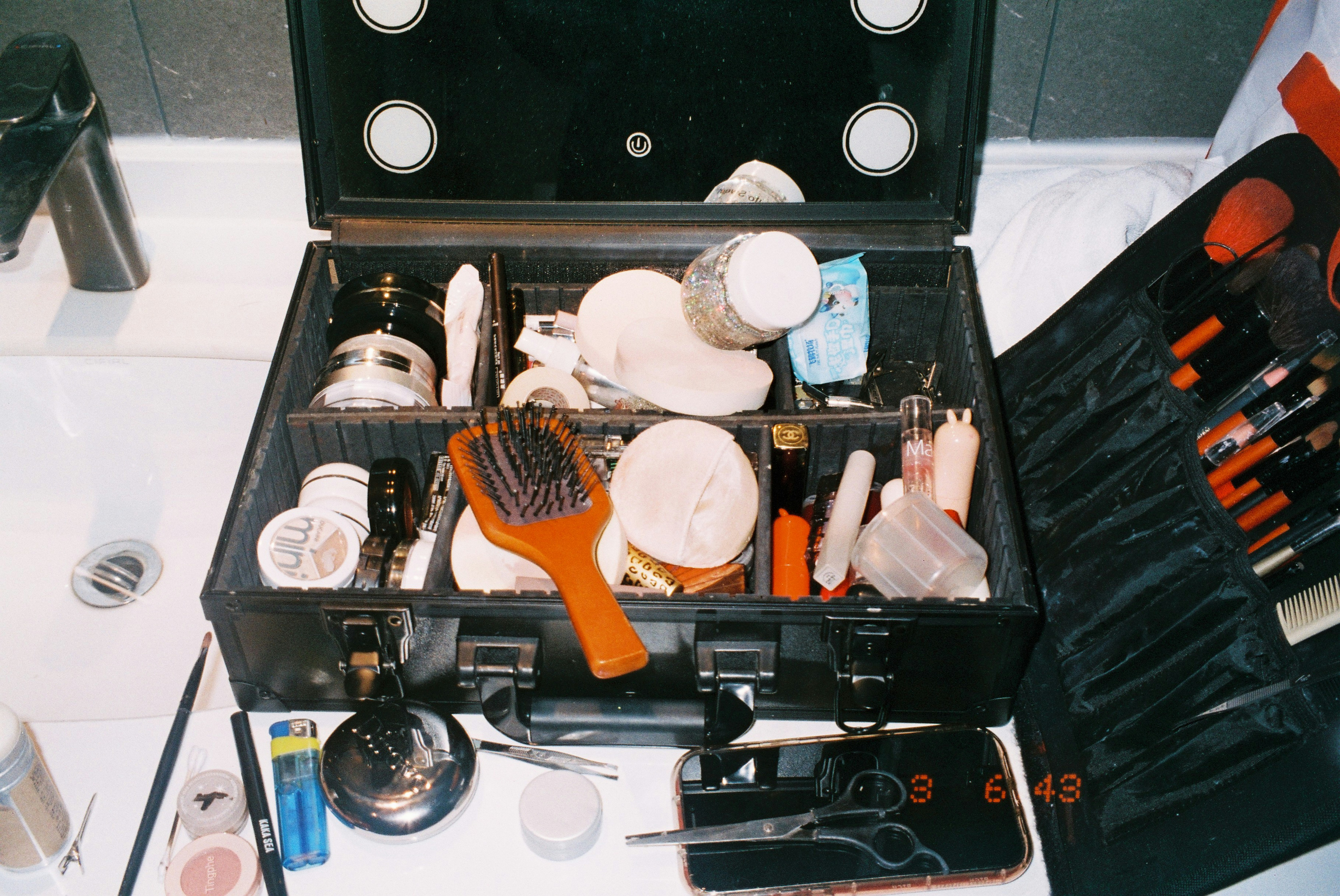 A black makeup case filled with brushes, sponges, and cosmetics on a bathroom counter