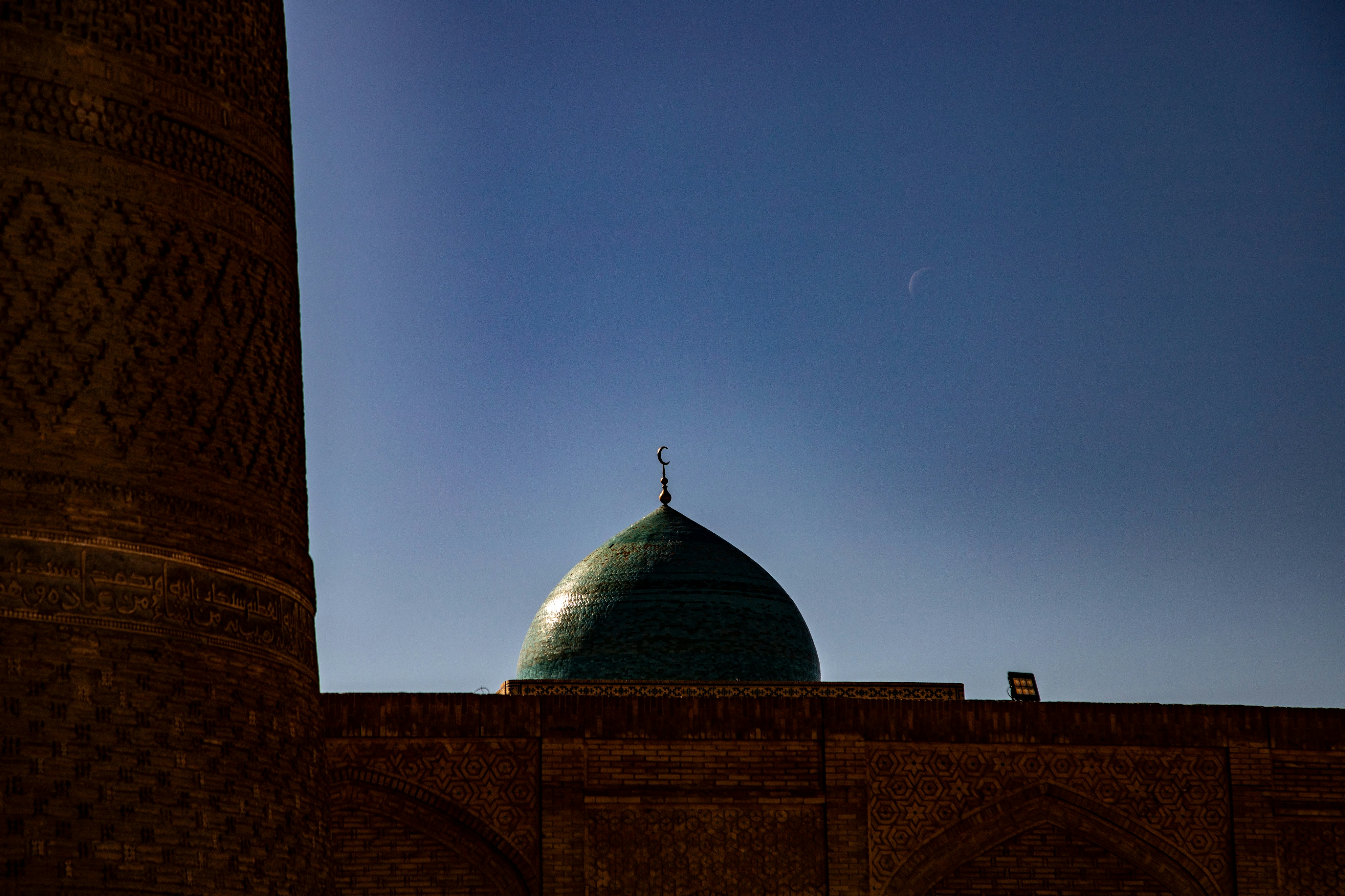 A turquoise dome with a crescent finial against a deep blue sky