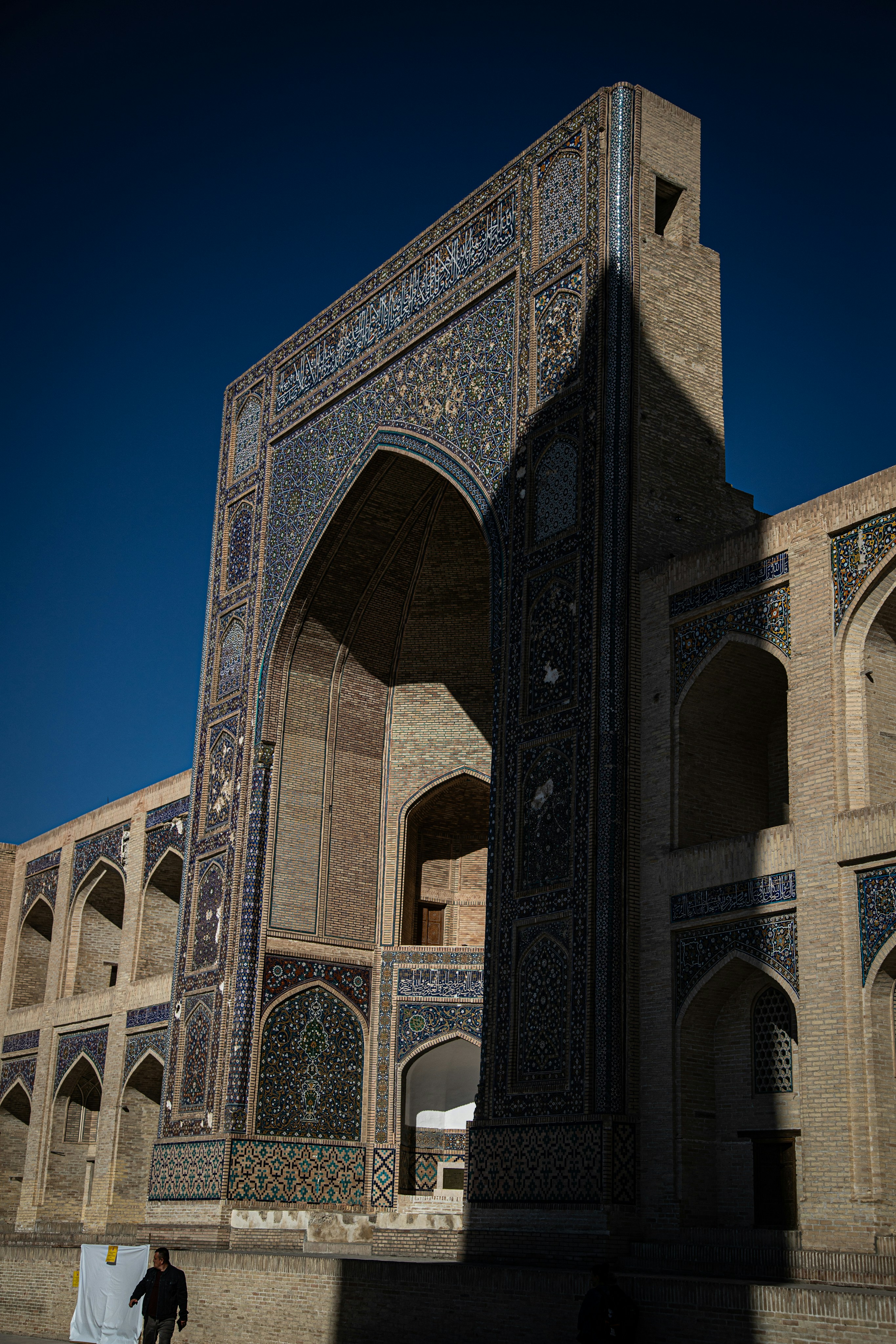 A person walking past the ornate tiled archway of the Mir-i-Arab Madrasah in Bukhara