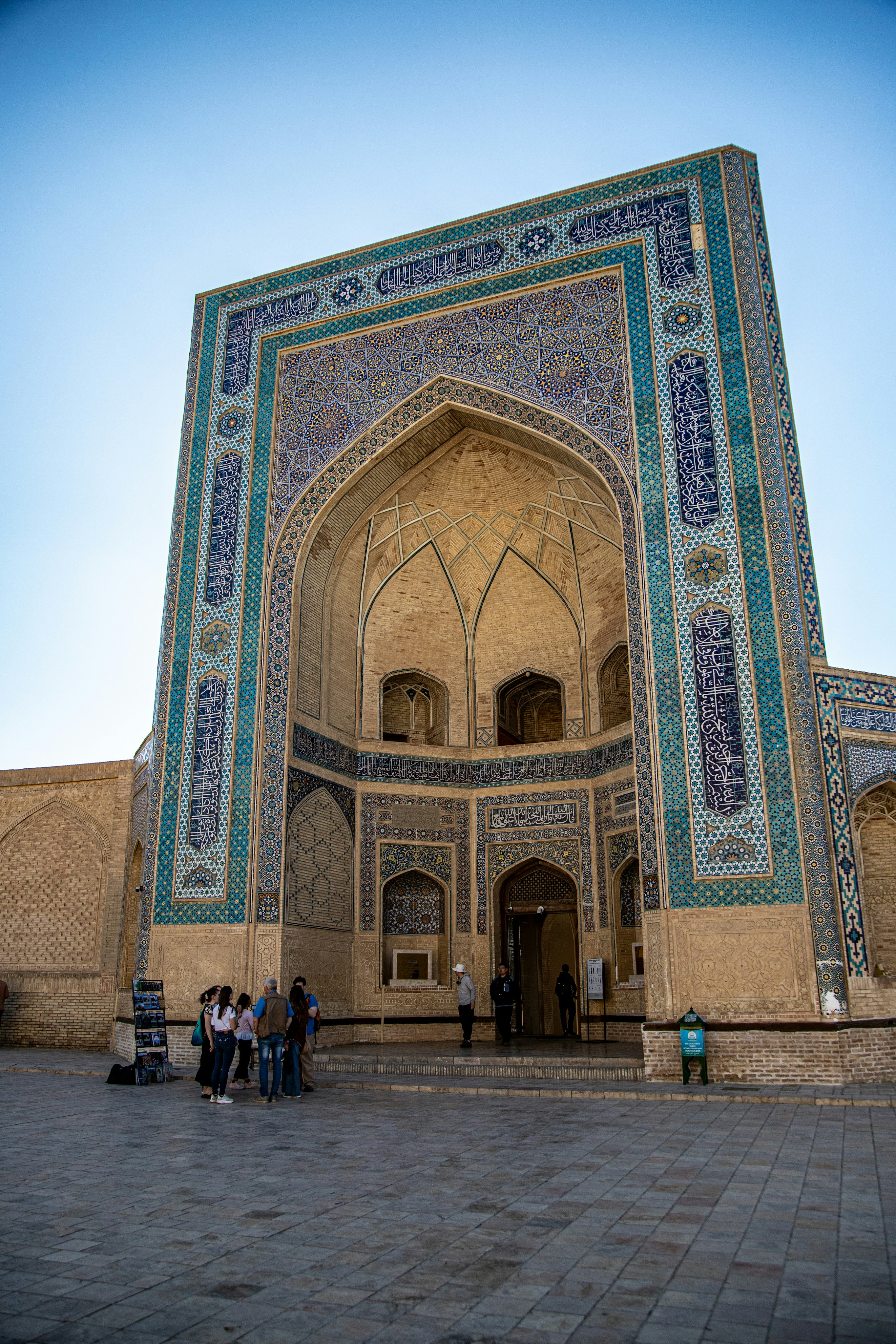 A group of people standing before the ornate blue tiled entrance of a madrasa