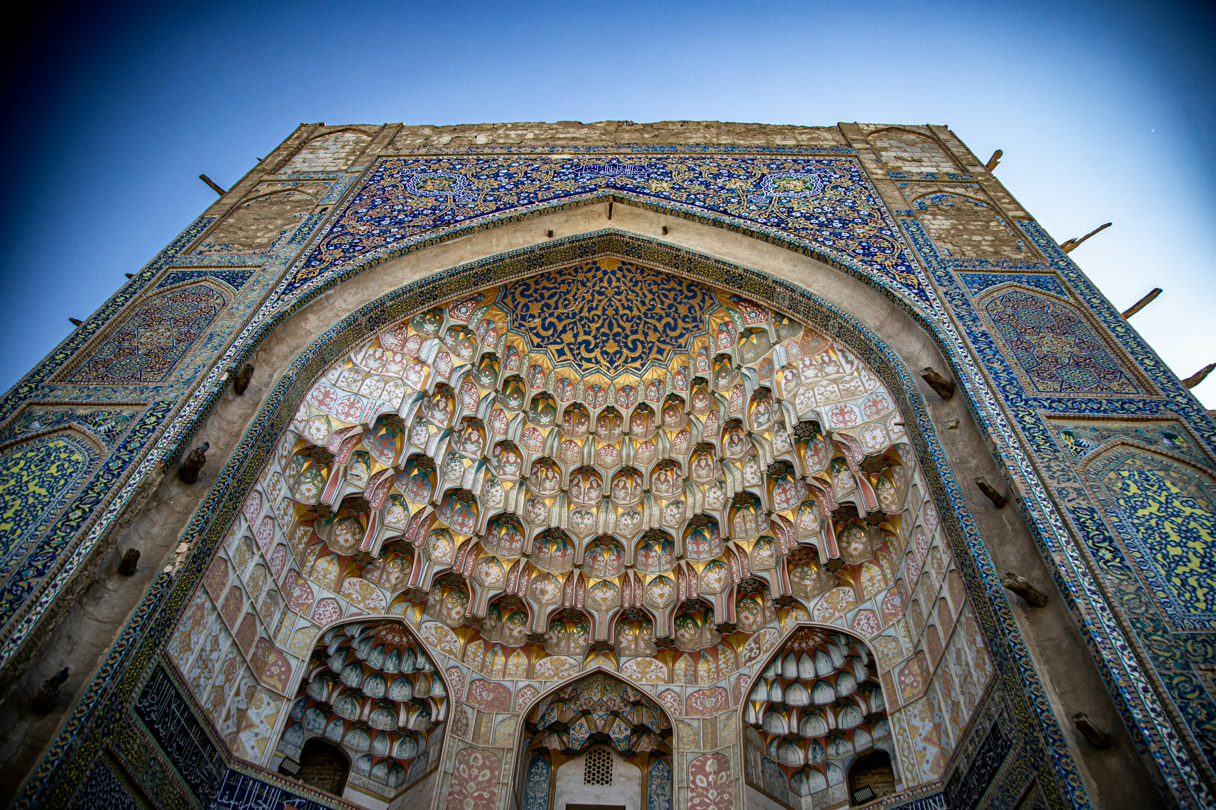 An ornate arched entrance with intricate blue tilework and golden honeycomb muqarnas vaulting