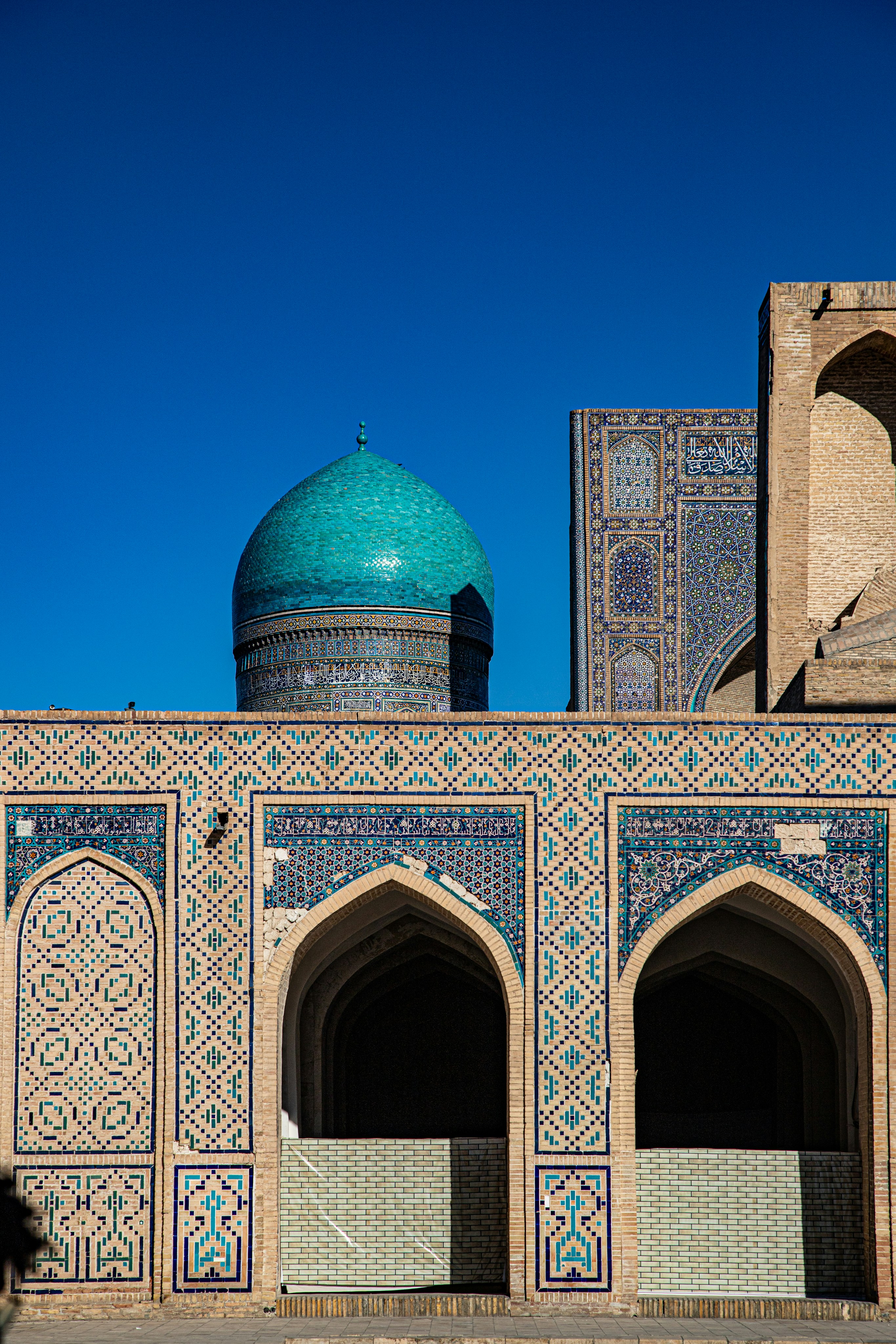 A turquoise dome rising above an arched brick building with intricate blue tilework