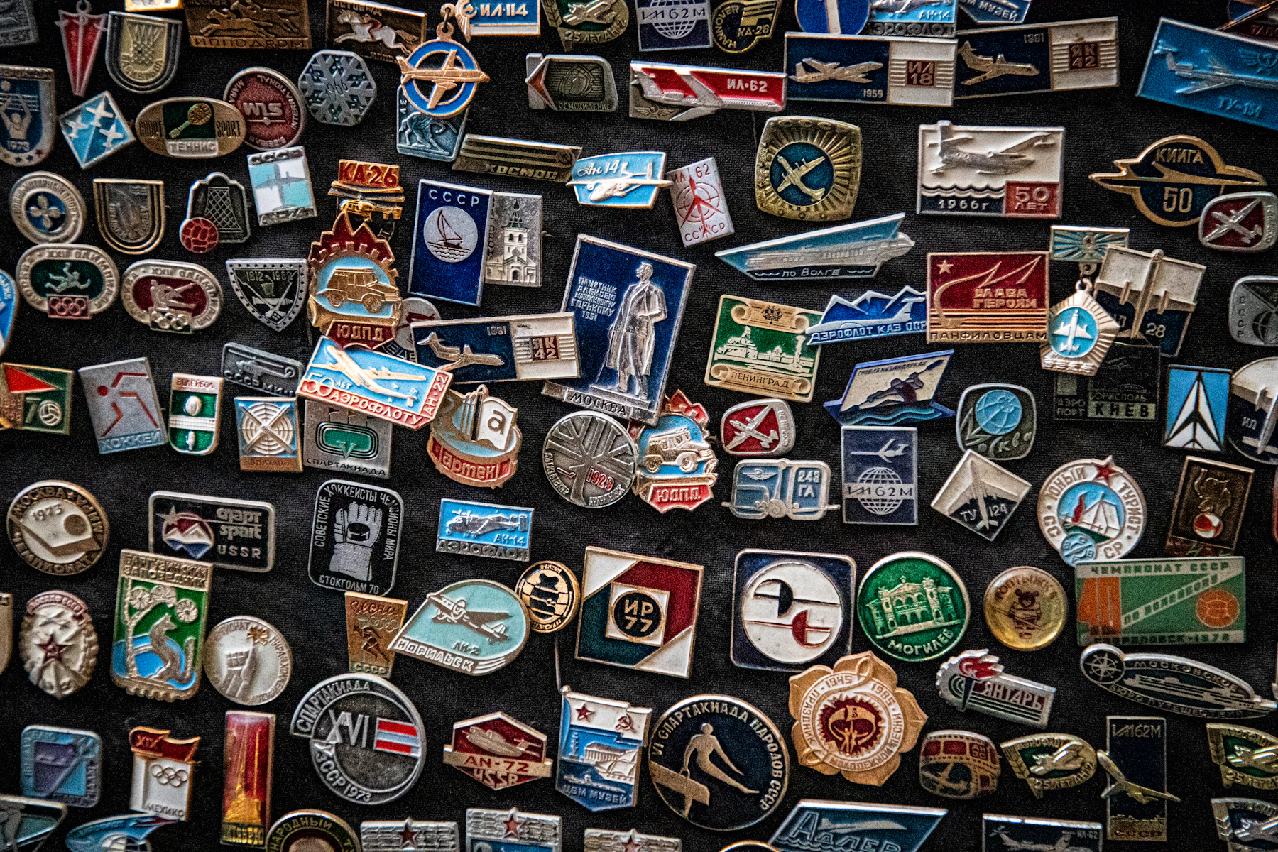 Rows of vintage Soviet enamel badges with aircraft and emblems laid out on black cloth