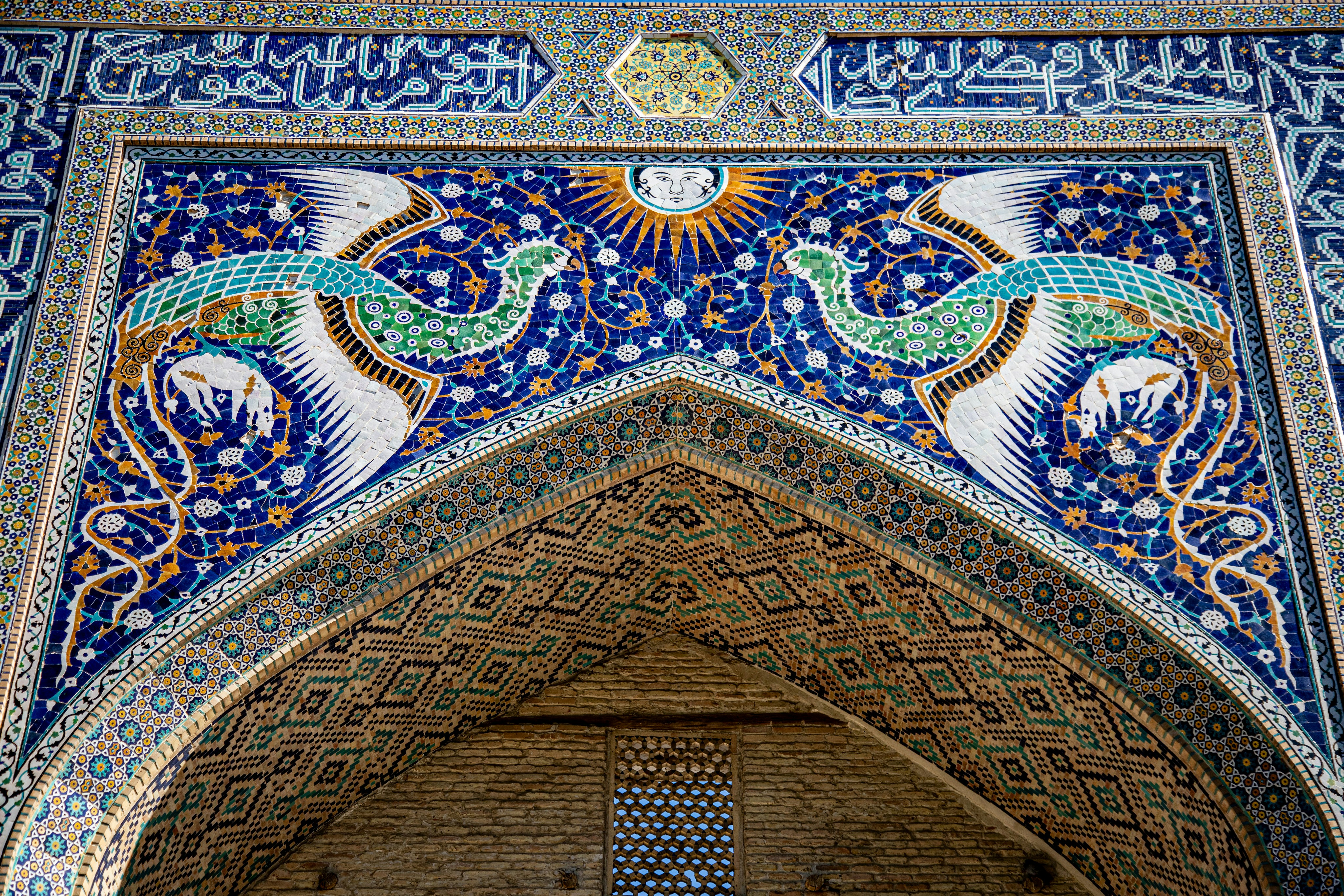 Intricate blue and green tile mosaic of two birds flanking a sun face