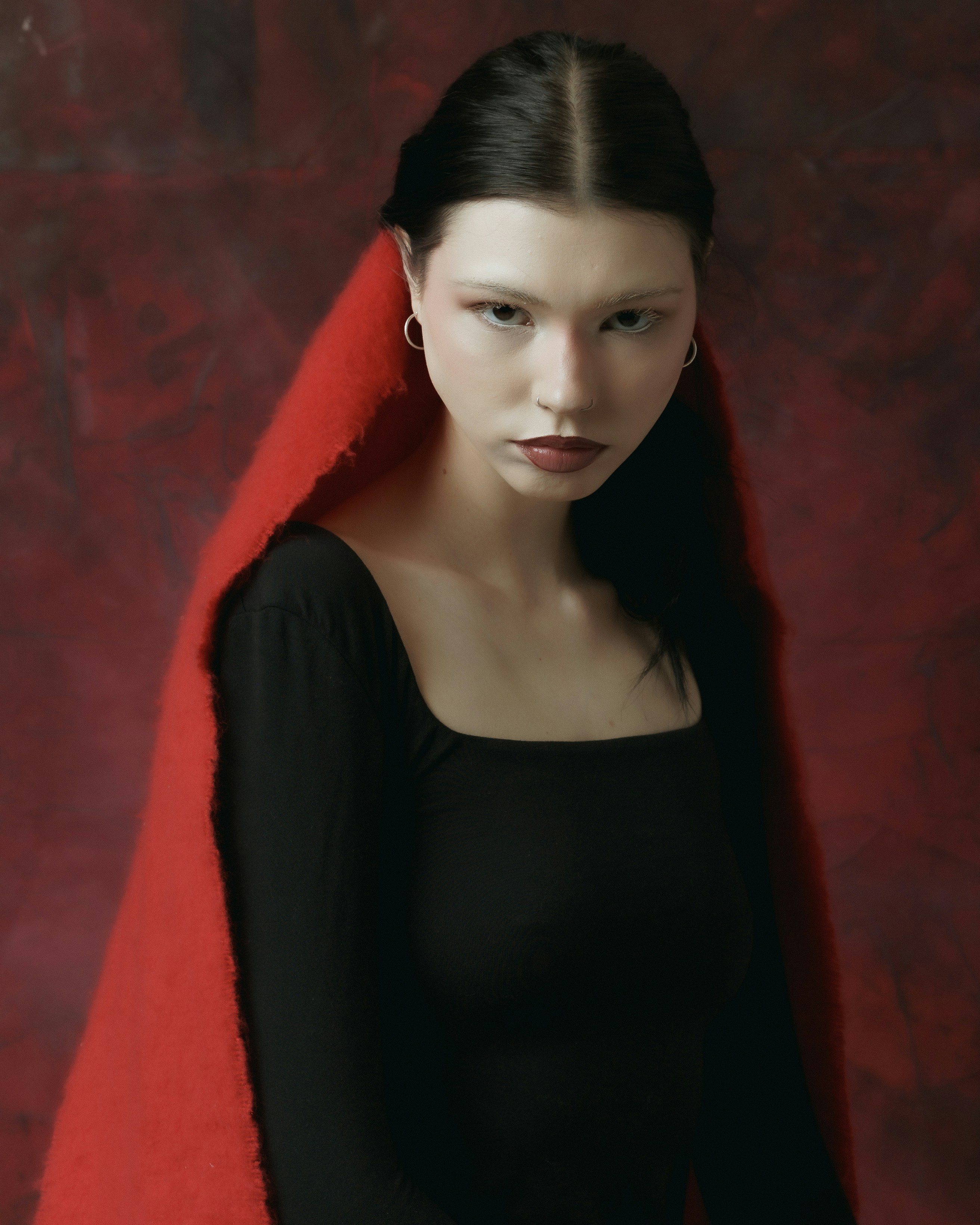 A woman in a black top draped in red fabric against a textured red wall