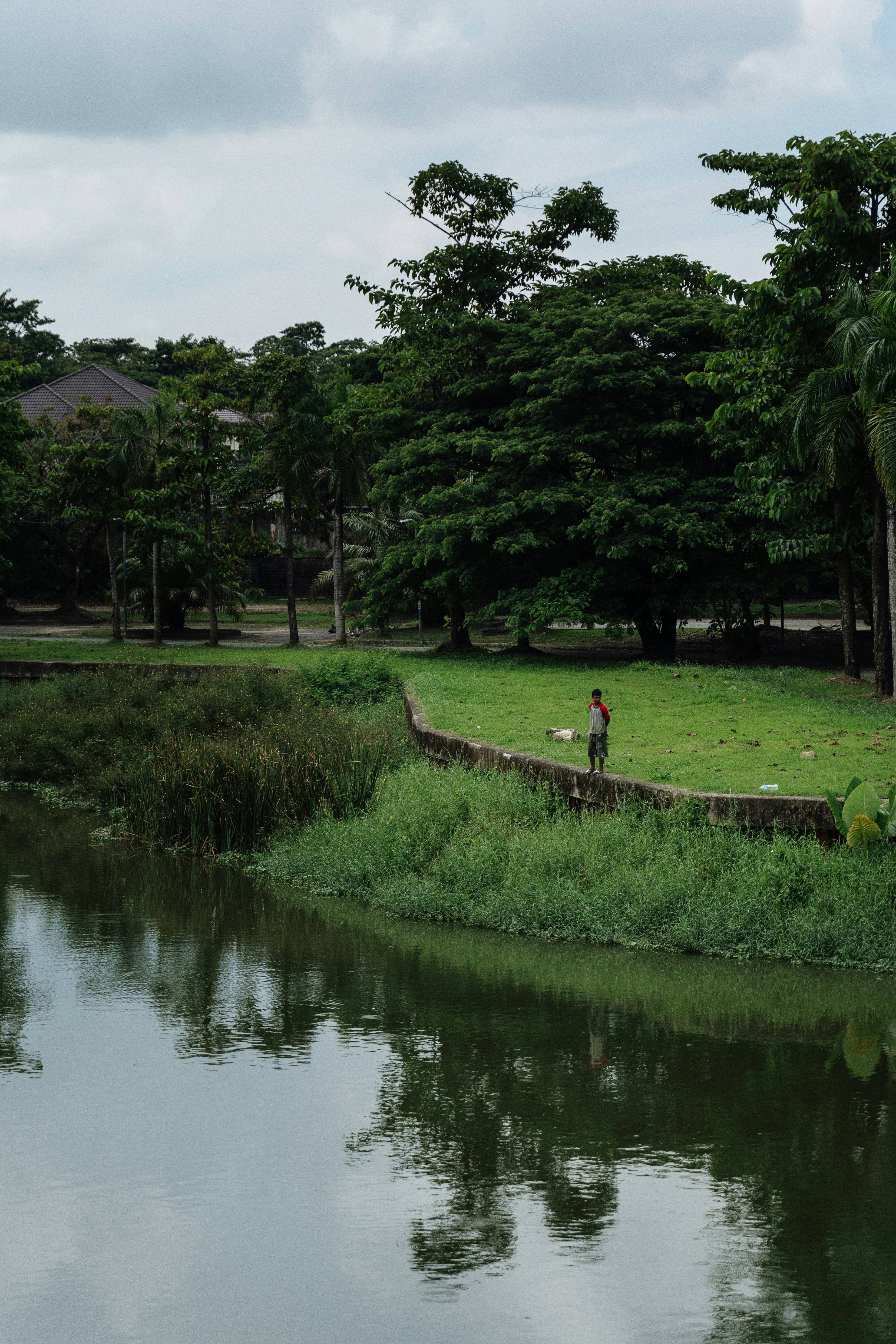 A person in a red and white shirt on a concrete wall beside a pond