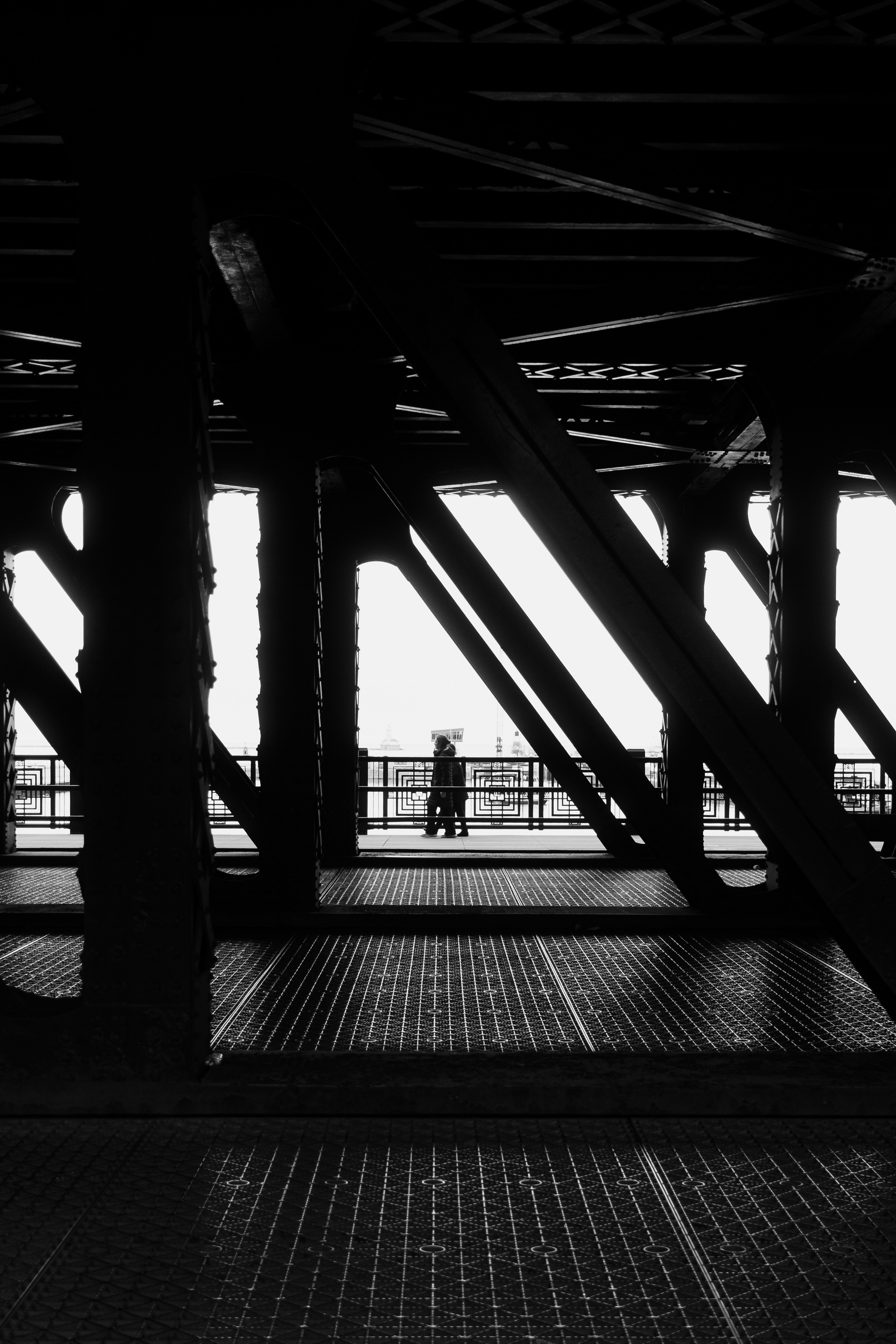 A person walking on a metal bridge walkway framed by dark steel girders