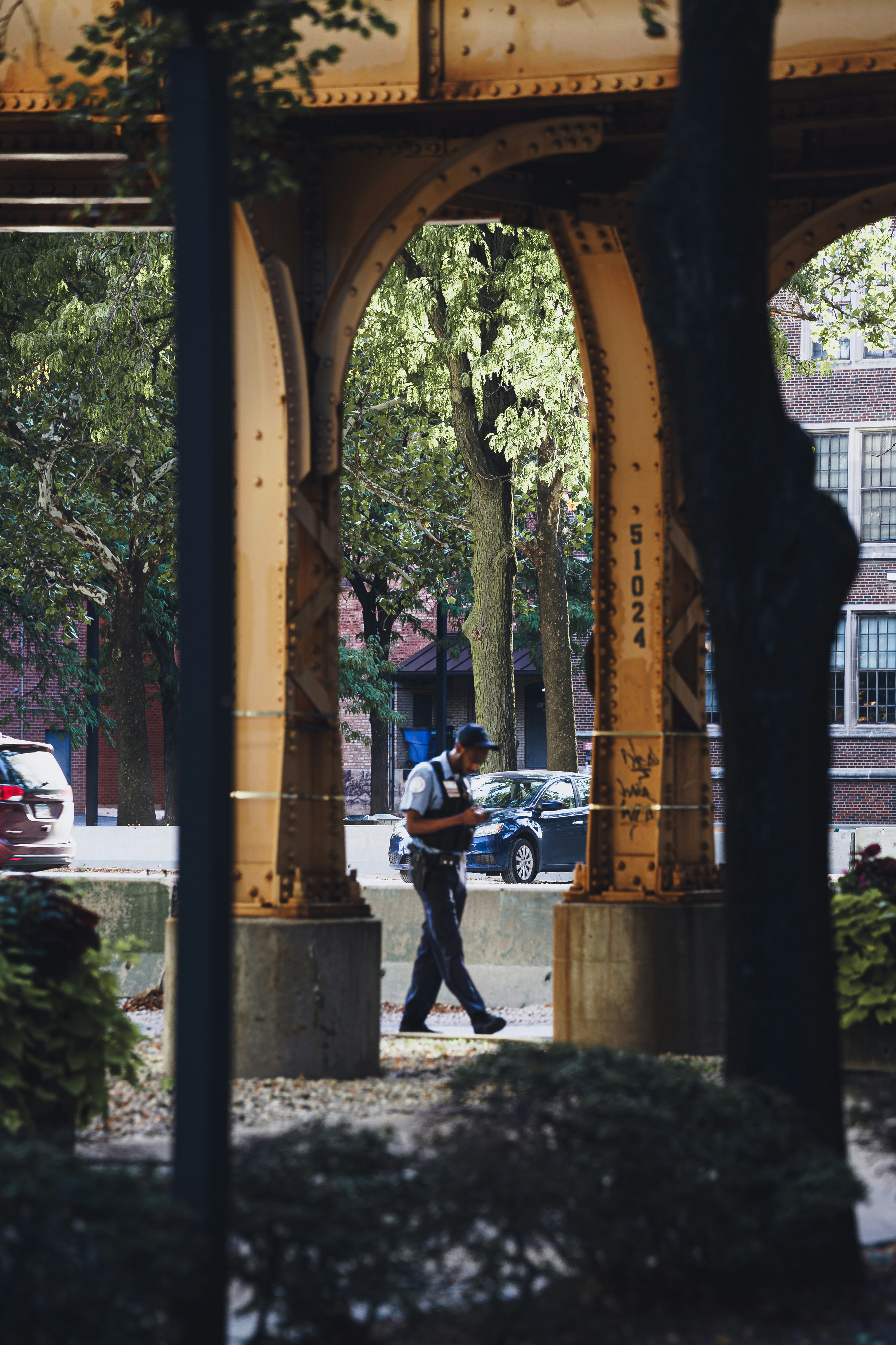 A person in a uniform walking past yellow steel bridge supports on a street