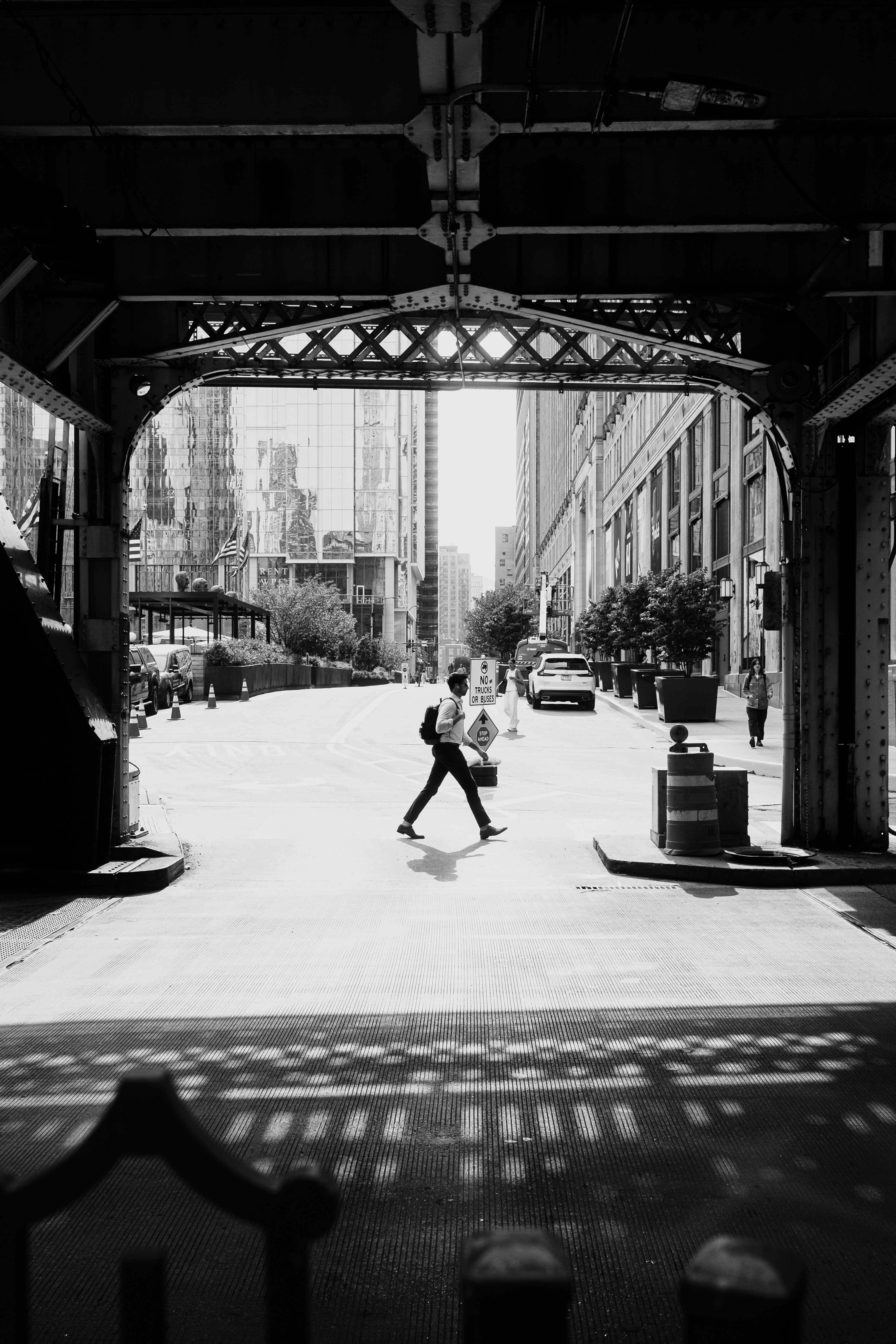 A person with a backpack walking across a city street under a bridge