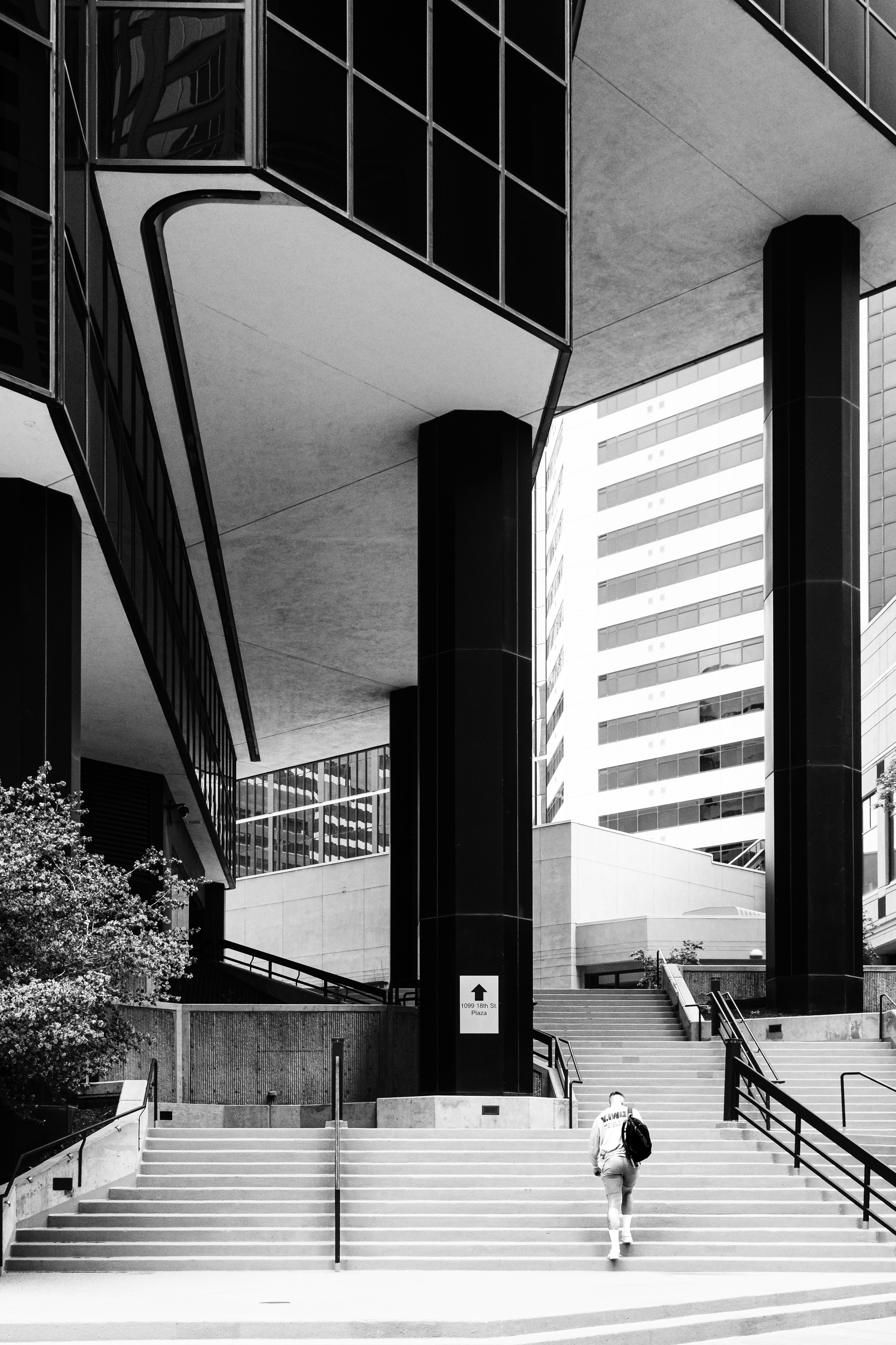 A person with a backpack walking up concrete stairs between modern office buildings