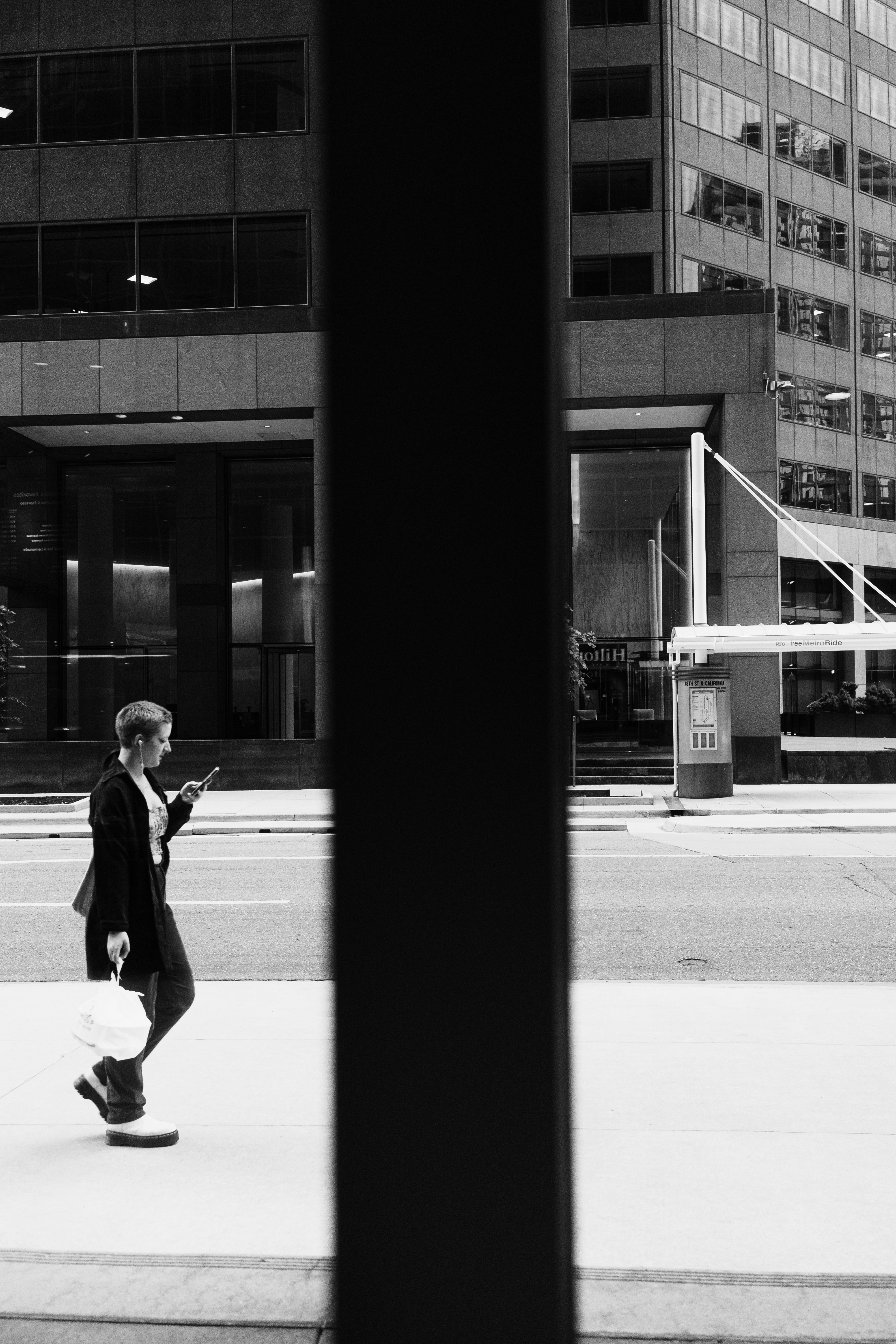 A person walking on a city sidewalk while looking at a smartphone