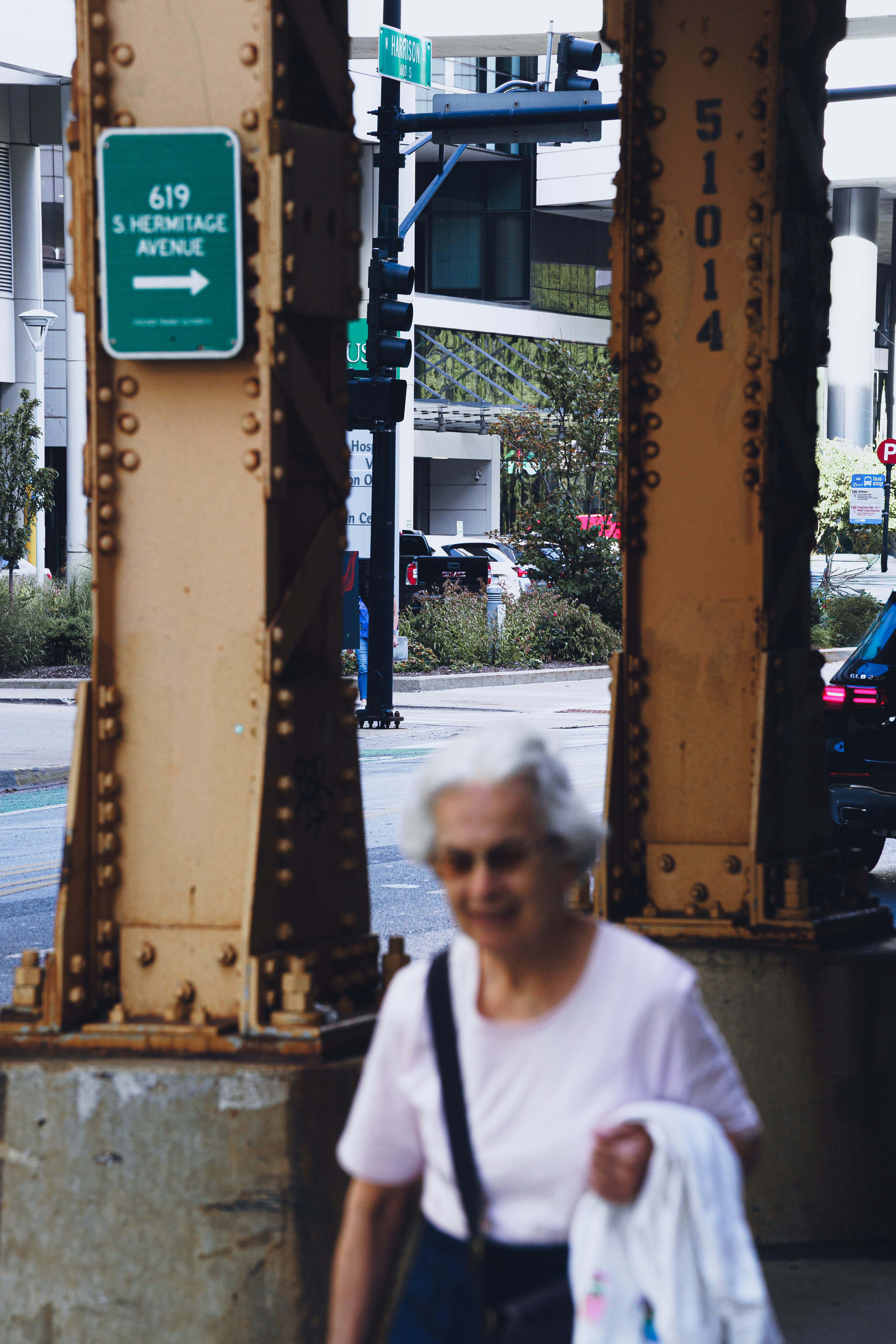 An older woman walking past yellow steel bridge supports on a city street