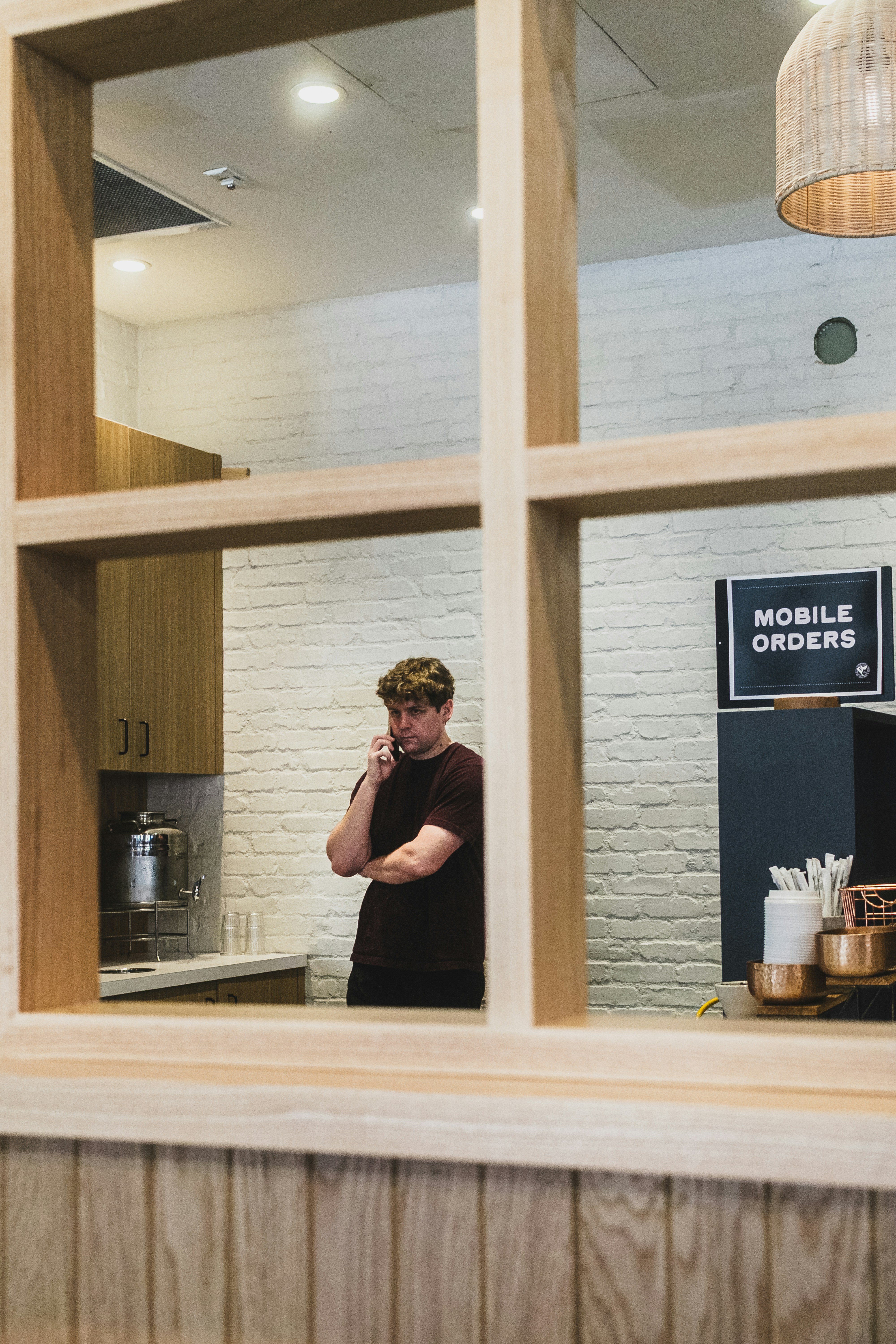 A person in a maroon t-shirt talking on a phone in a cafe