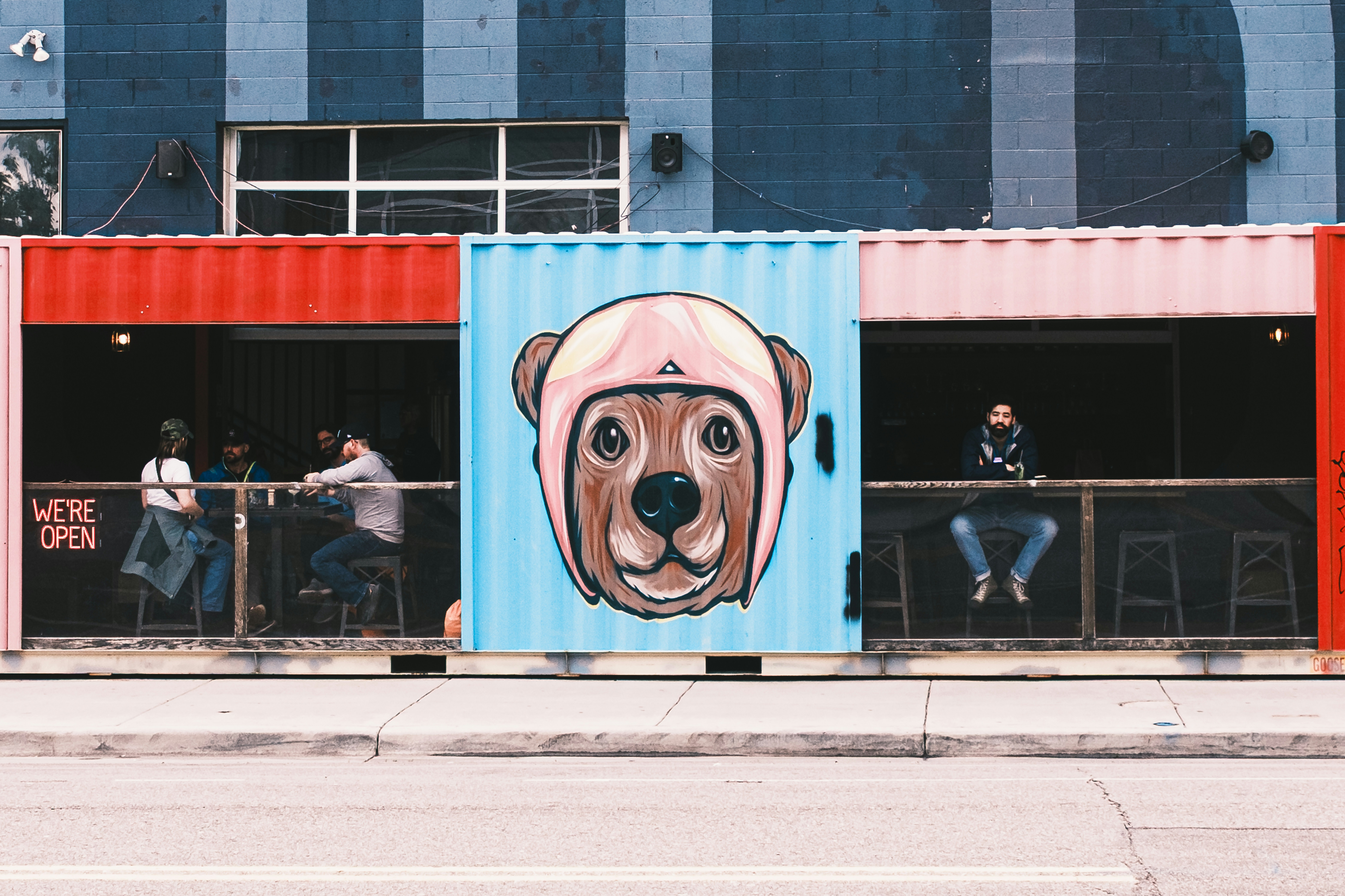 People sitting at tables in a shipping container cafe with a bear mural