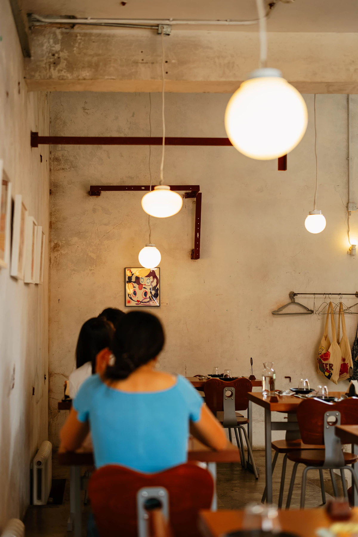 Orang-orang duduk di meja kayu kafe dengan lampu gantung bulat