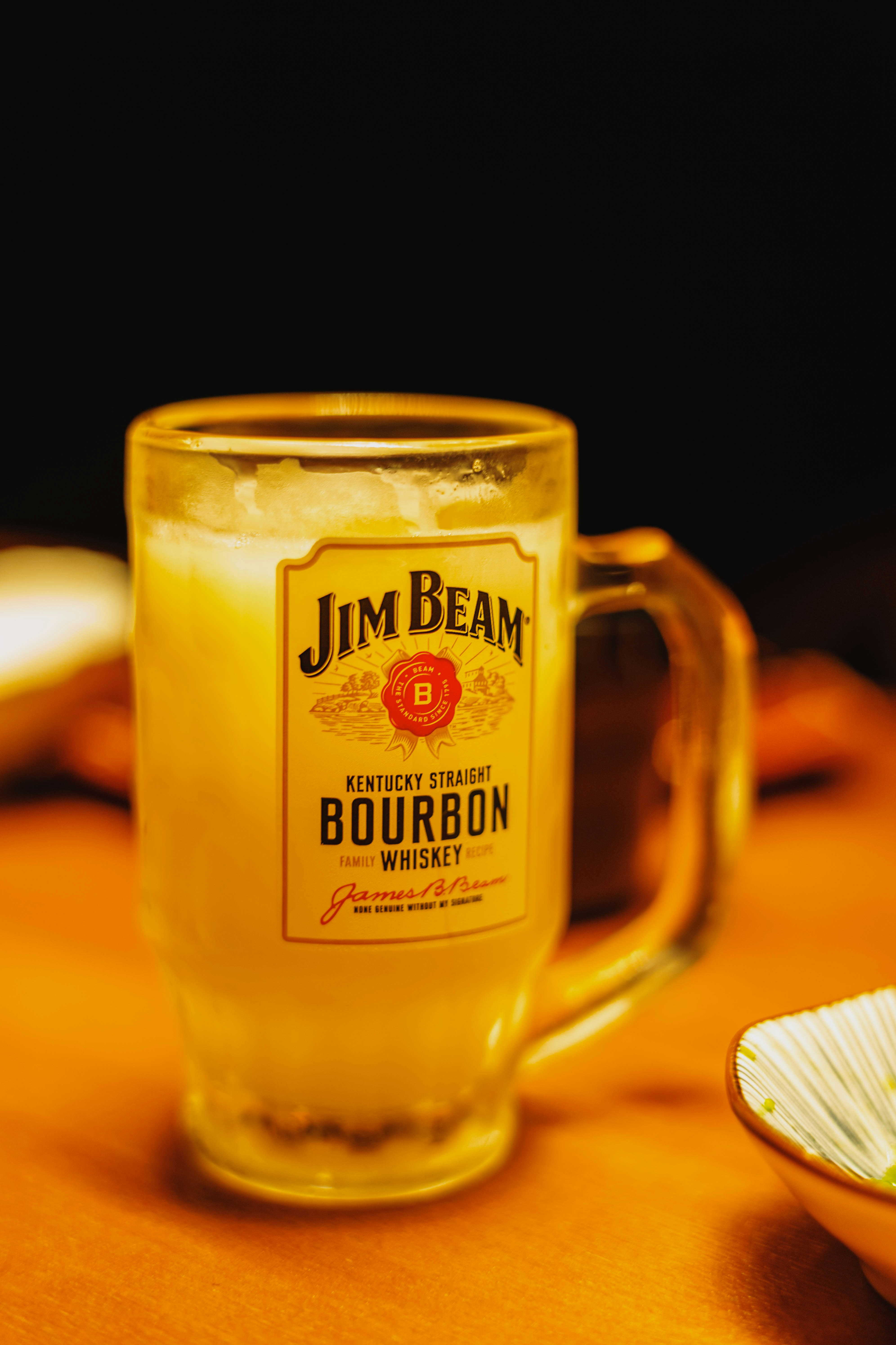 黄色い飲み物が入ったガラスのマグカップとジム・ビームのラベル