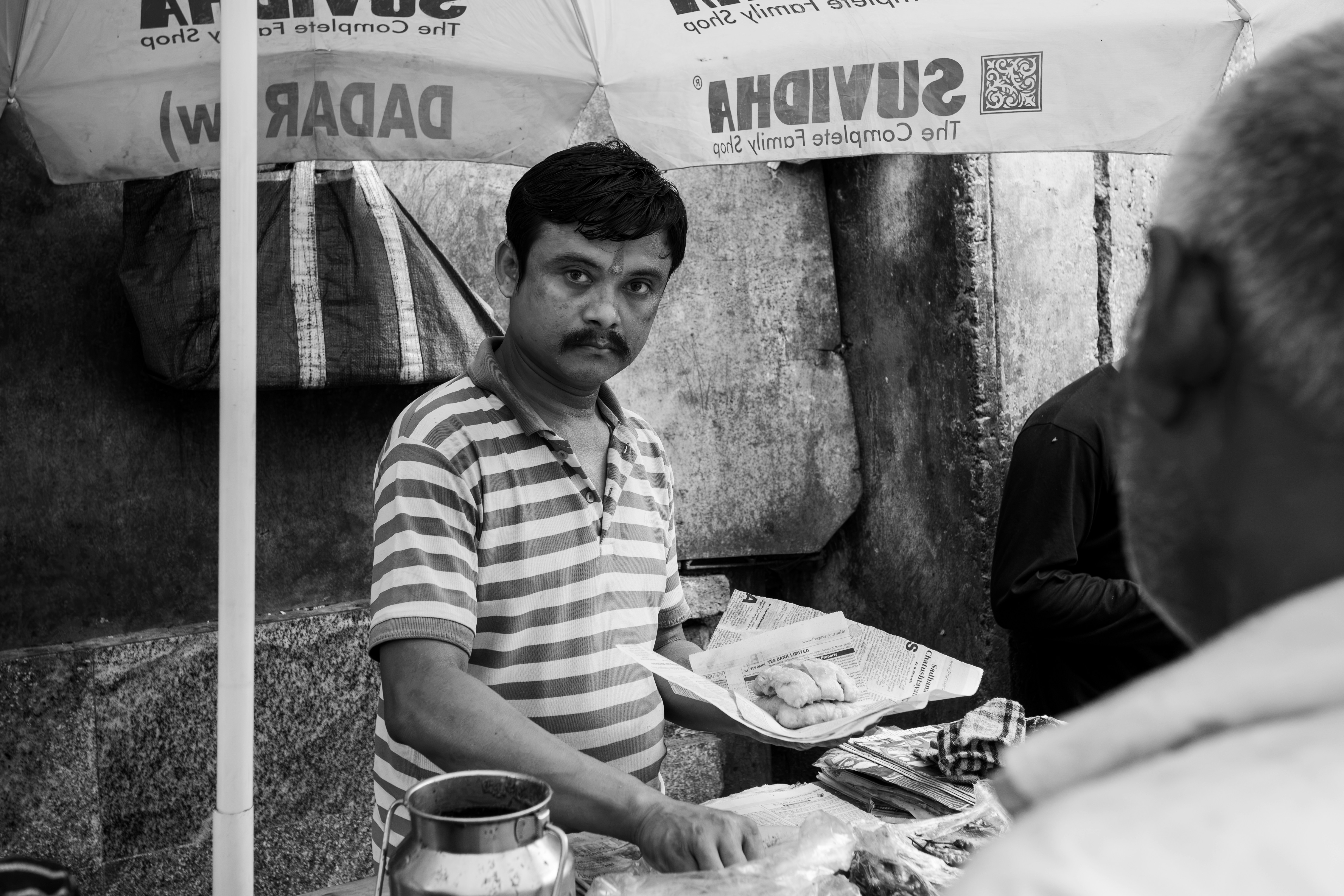 A man in a striped polo shirt serving food on newspaper under a branded umbrella