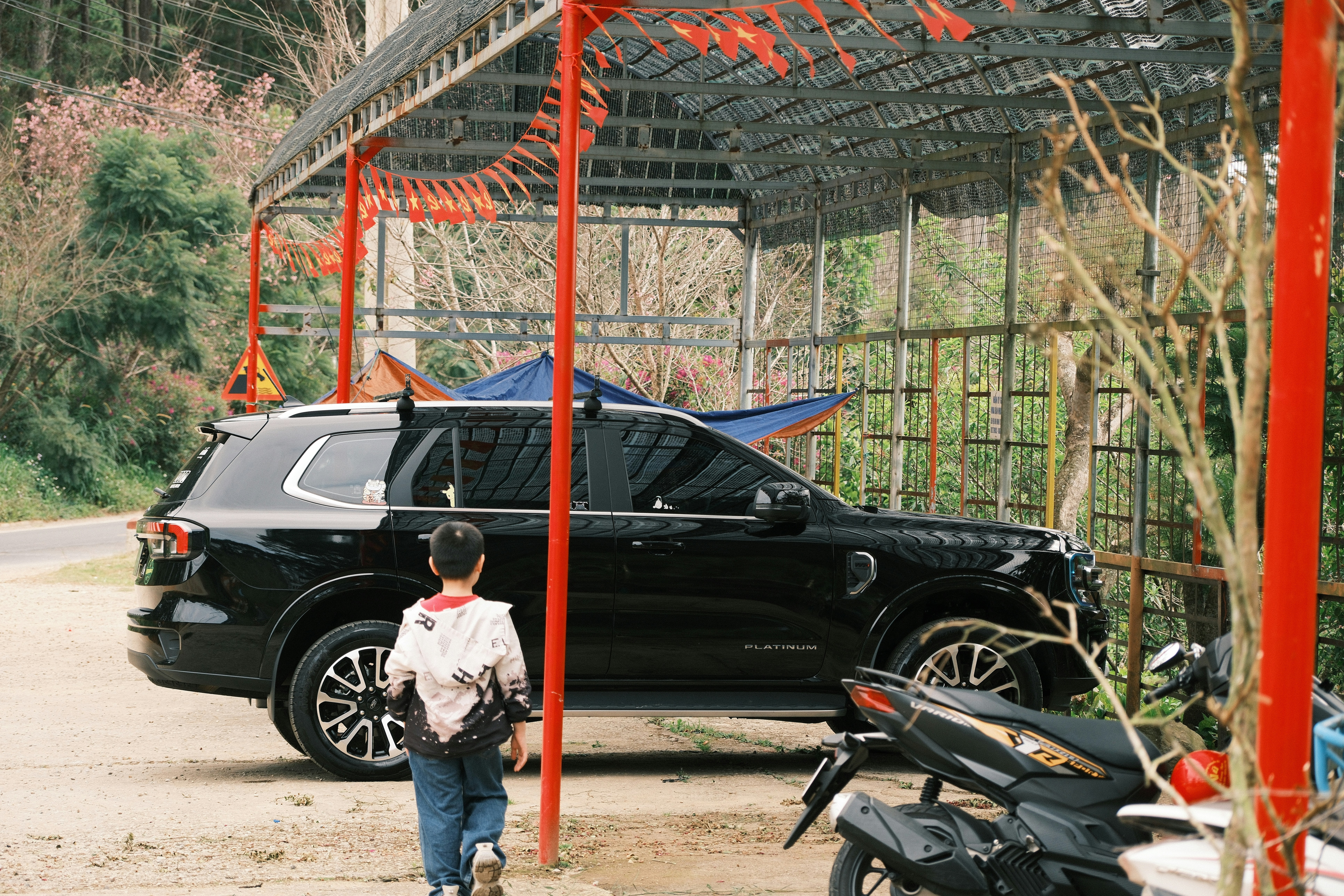 A child walking toward a black SUV parked under a red metal frame structure