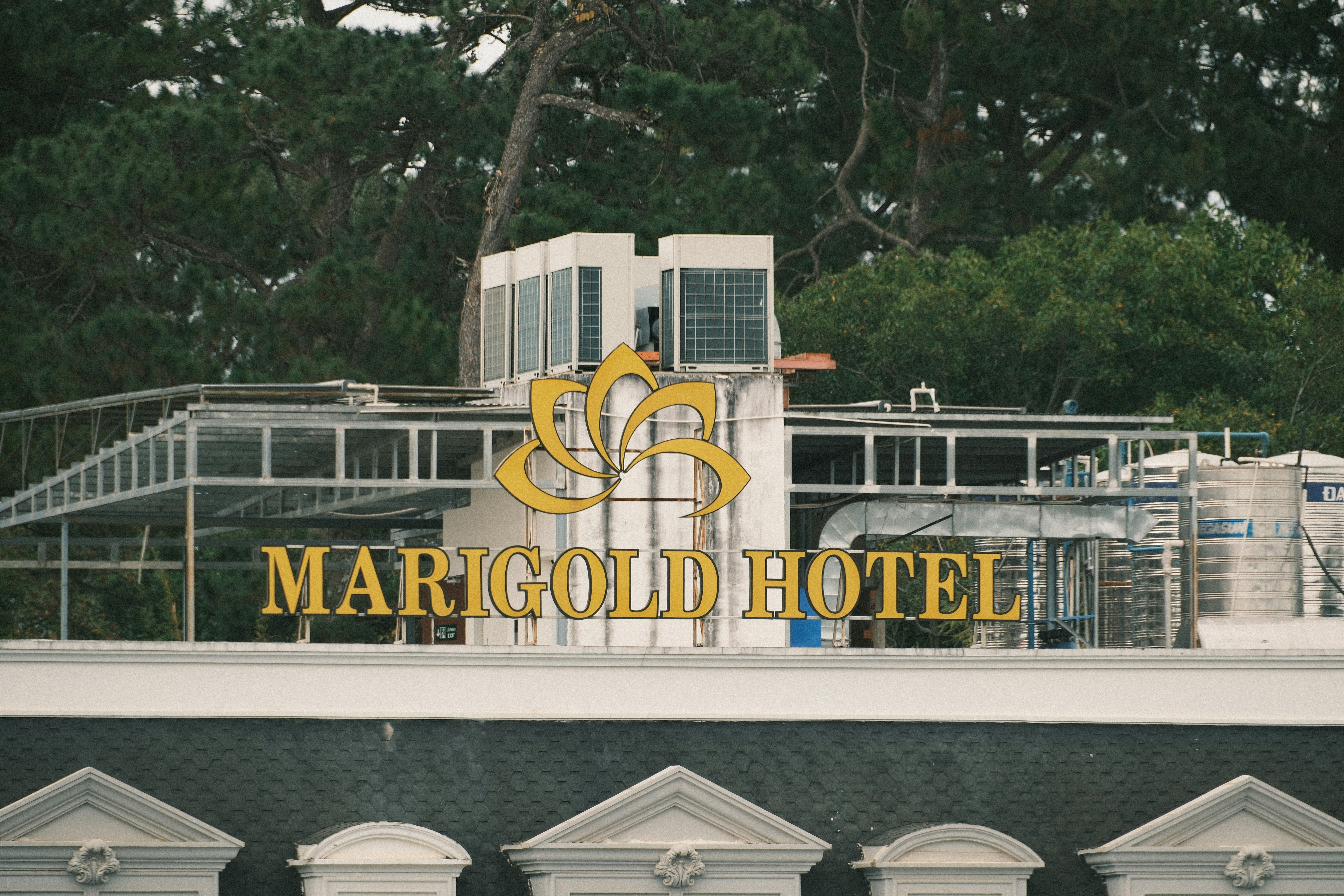A Marigold Hotel sign with a gold floral logo on a rooftop with industrial equipment