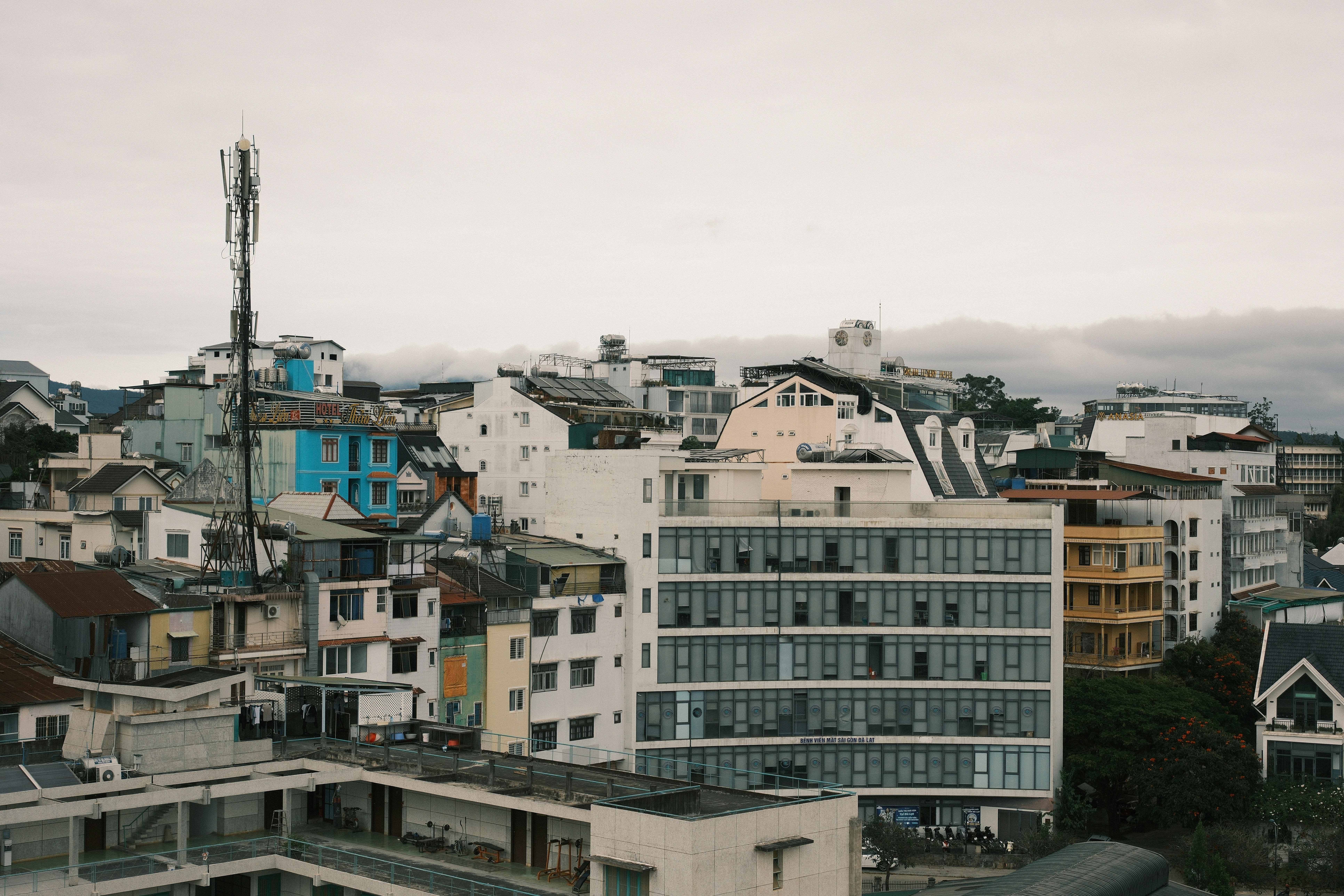 A dense cityscape of multi-story buildings with a tall telecommunications tower under a cloudy sky