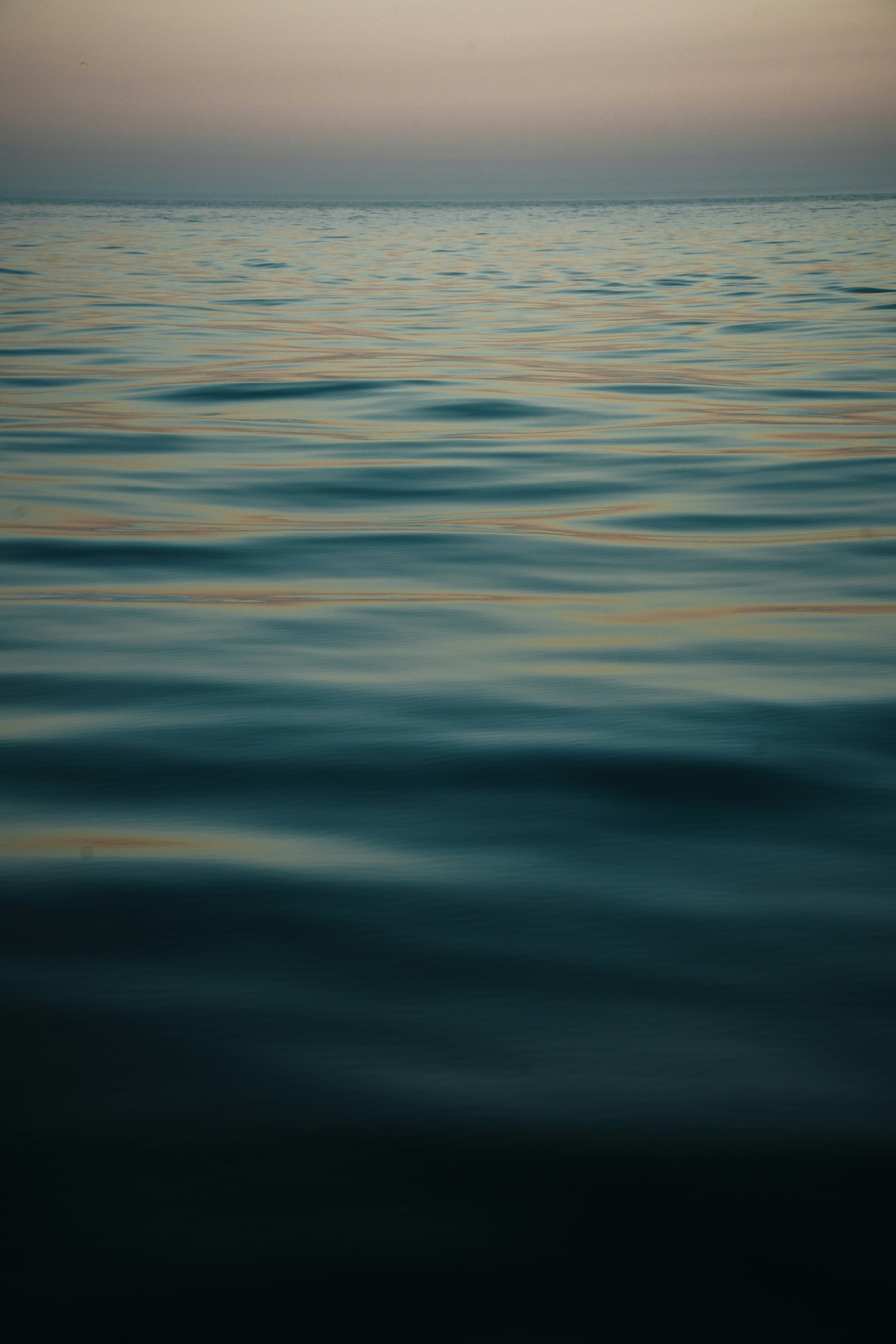 Gentle ripples on dark blue water reflecting soft light at the horizon