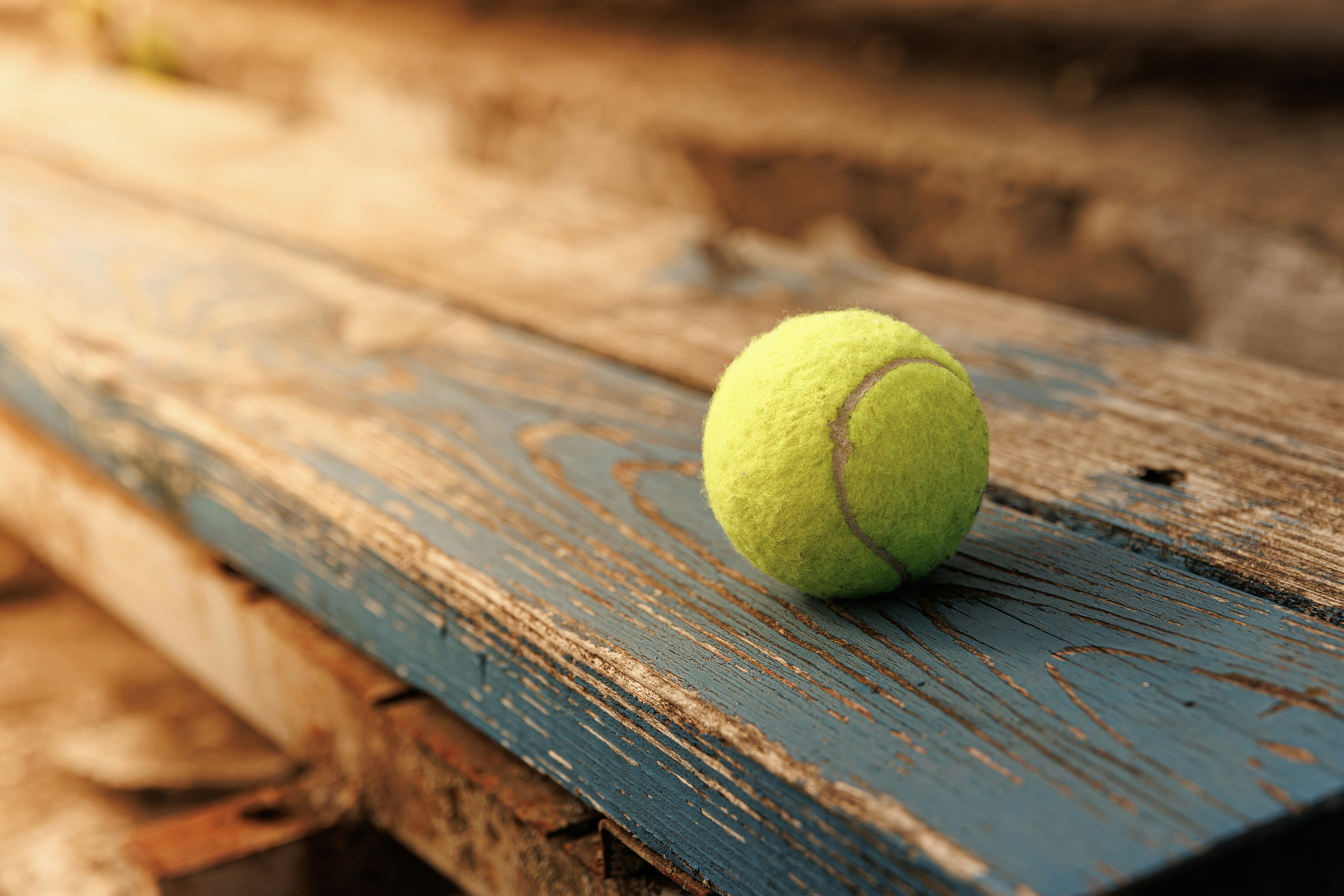 Ein gelber Tennisball auf einer verwitterten blauen Holzbank im warmen Licht