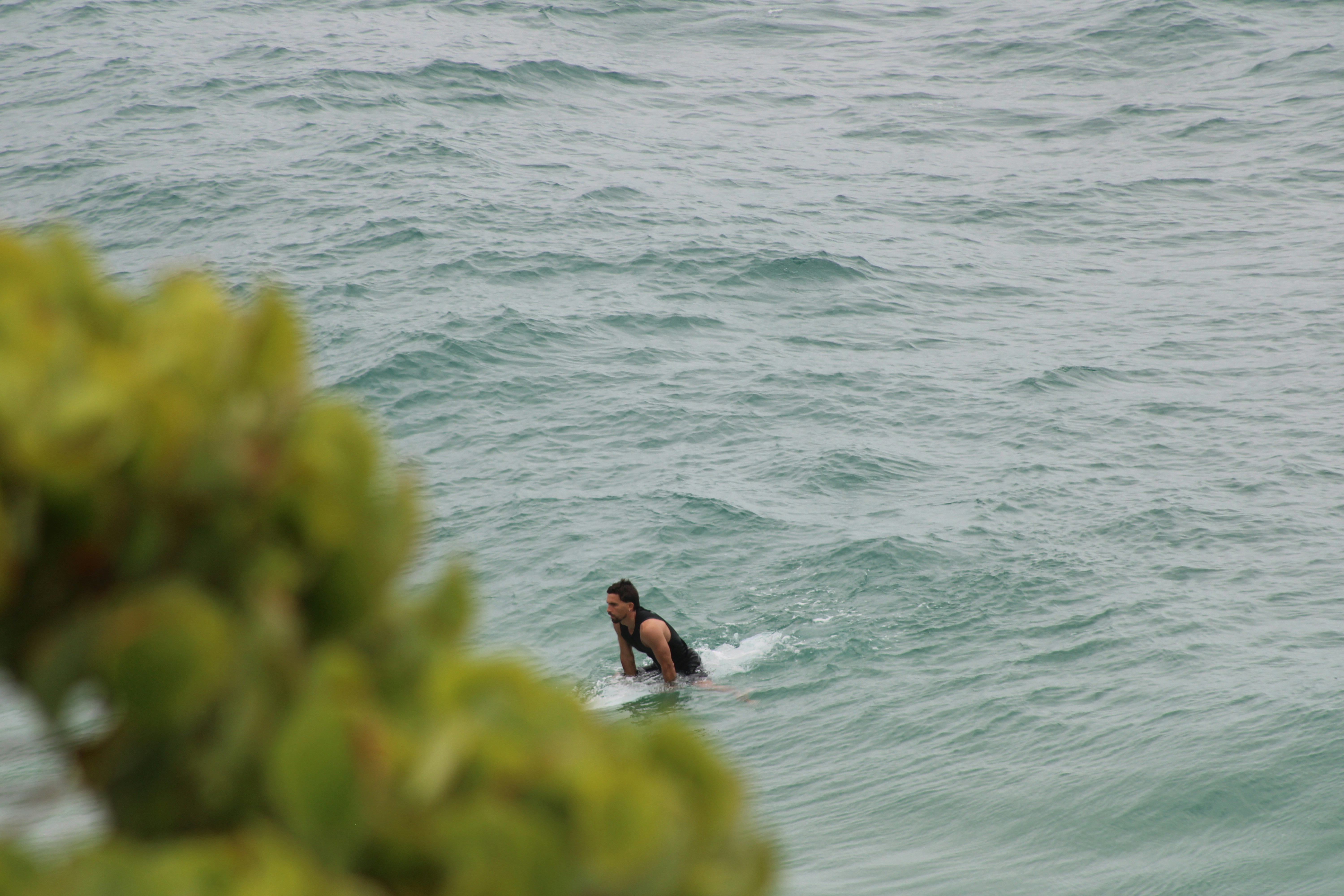 A man in a black wetsuit paddling on a surfboard in choppy ocean water