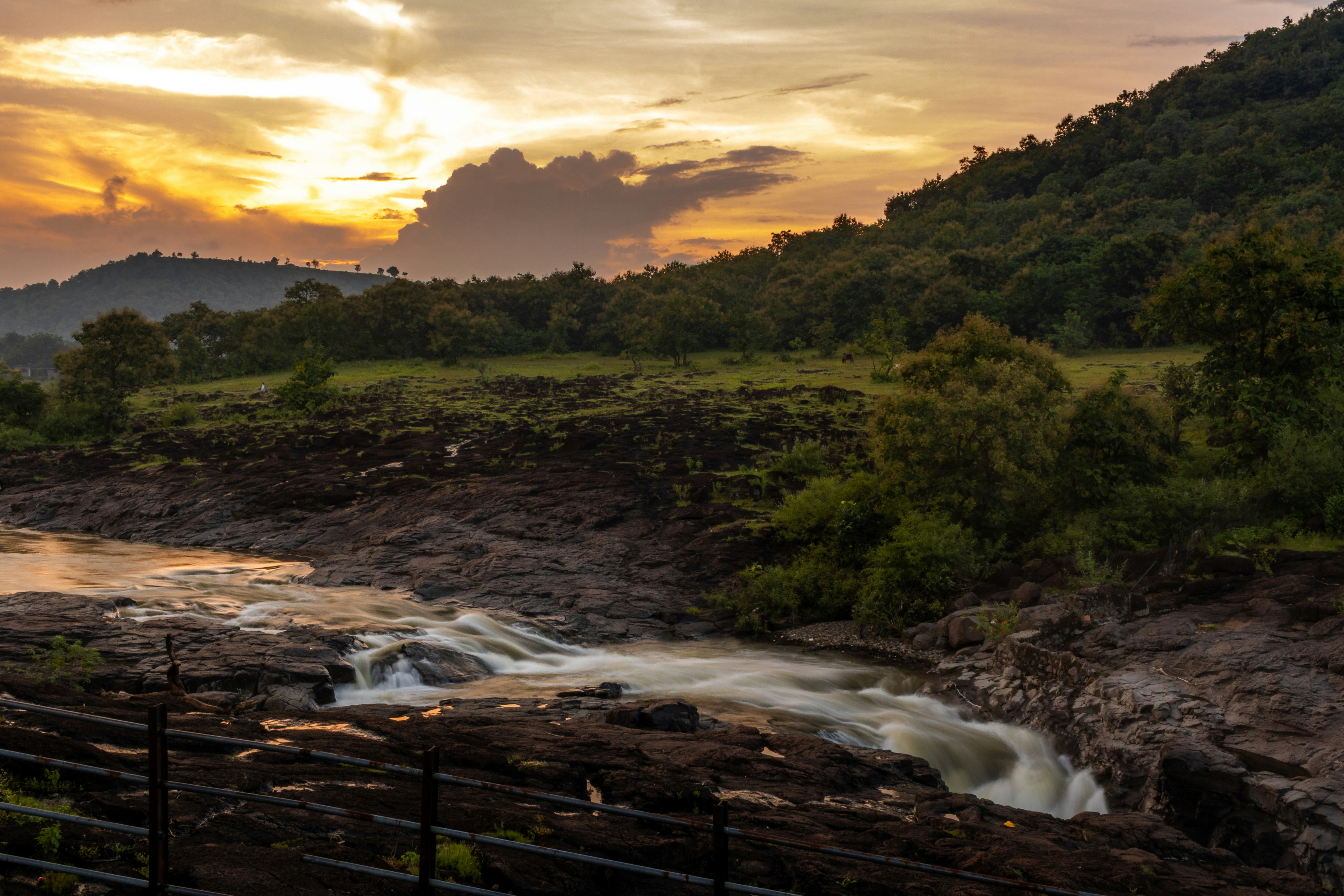 A river flowing over dark rocks through a green landscape under golden hour light
