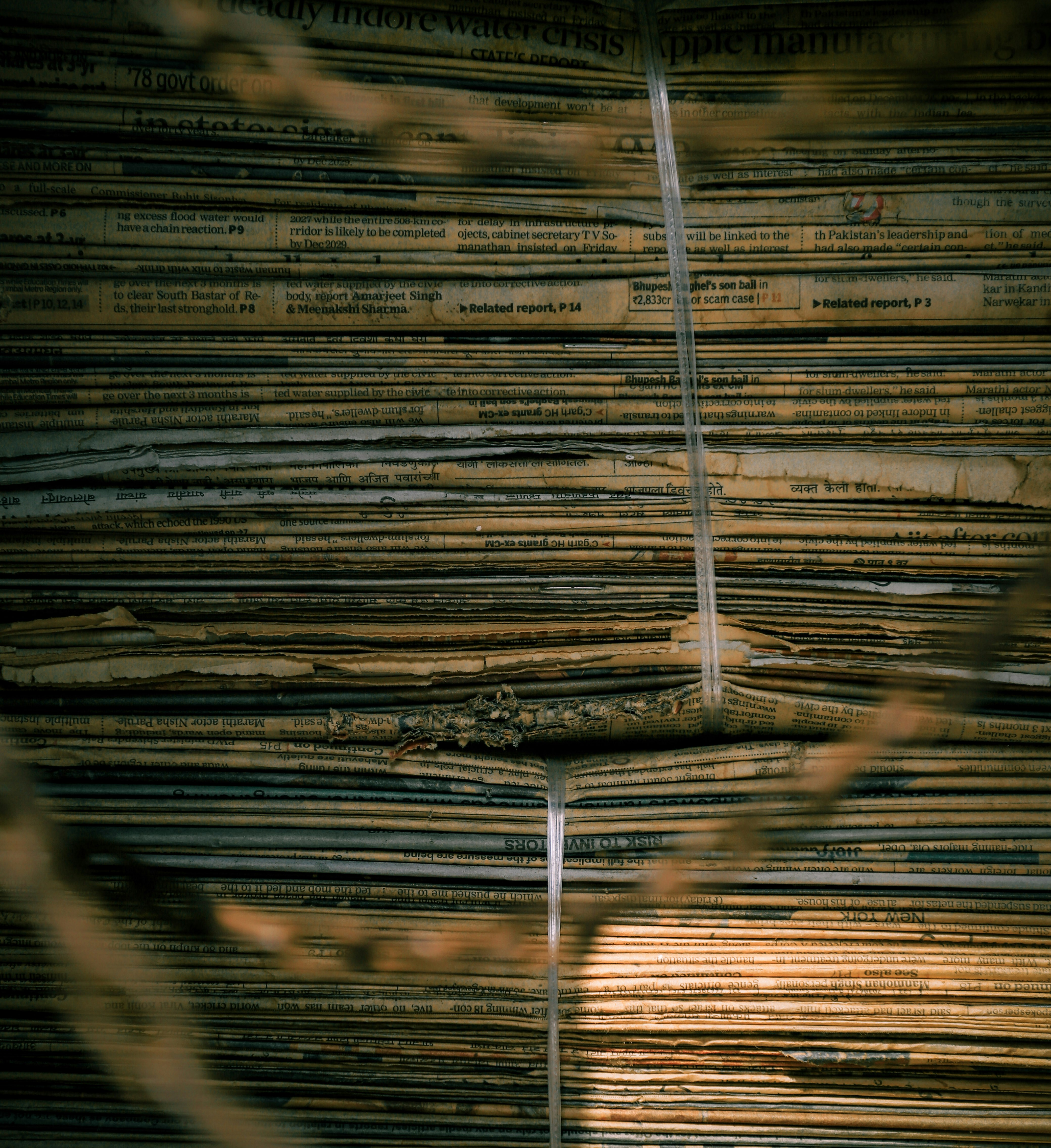 verbiage: A stack of old newspapers bound together with thin plastic twine in warm light