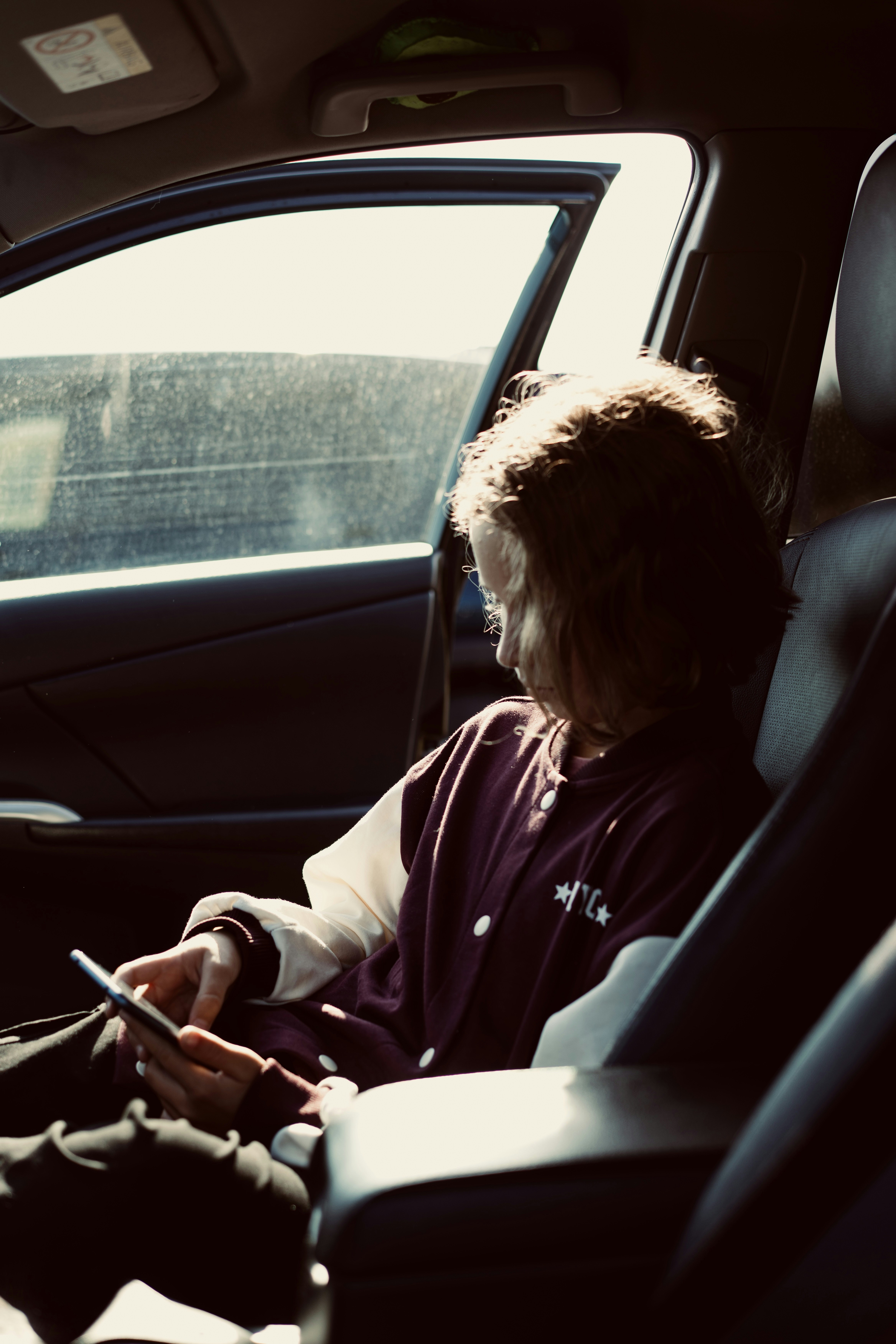 A person in a maroon and white varsity jacket using a smartphone in a car