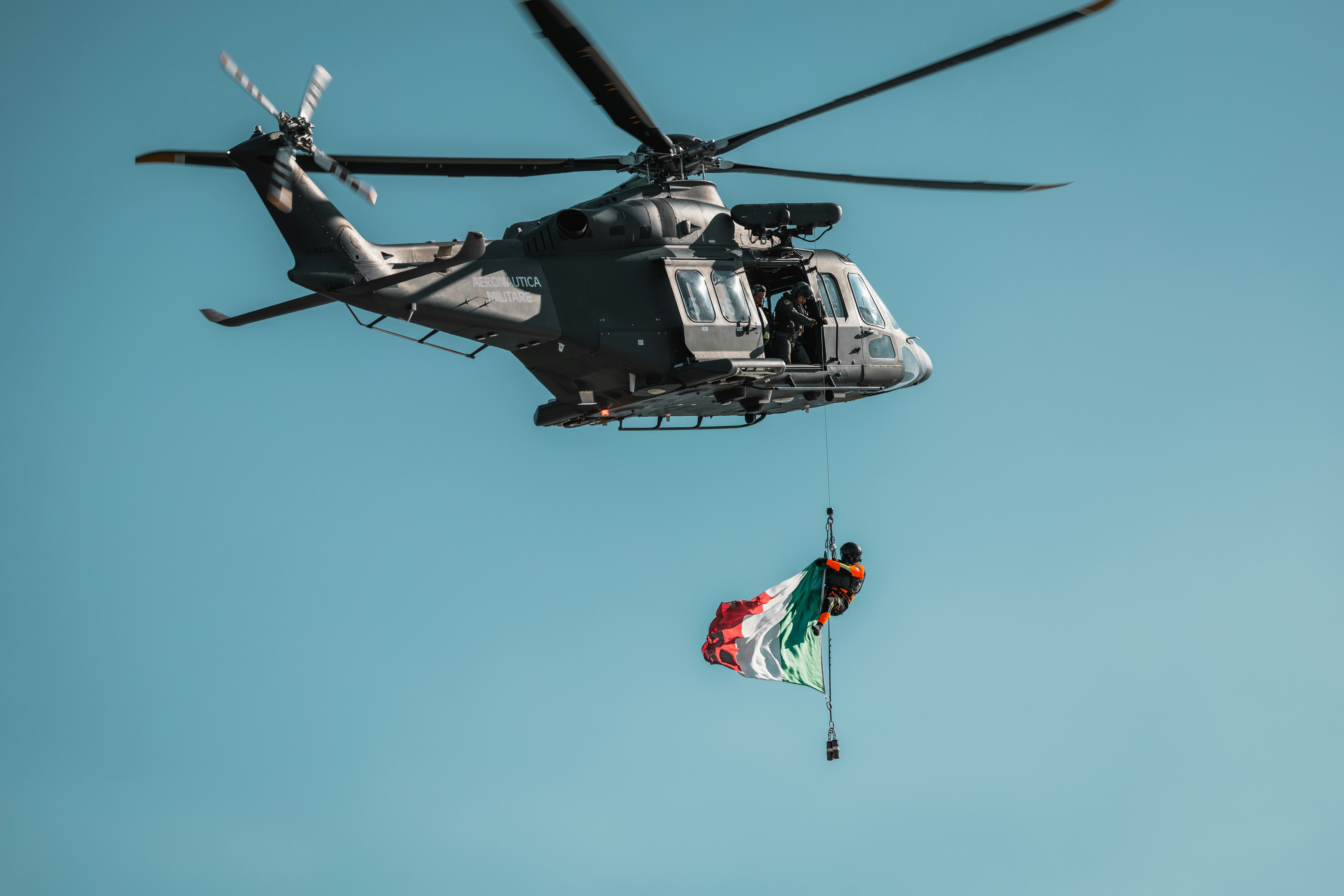 Seorang orang yang digantung dari helikopter militer yang memegang bendera besar Italia