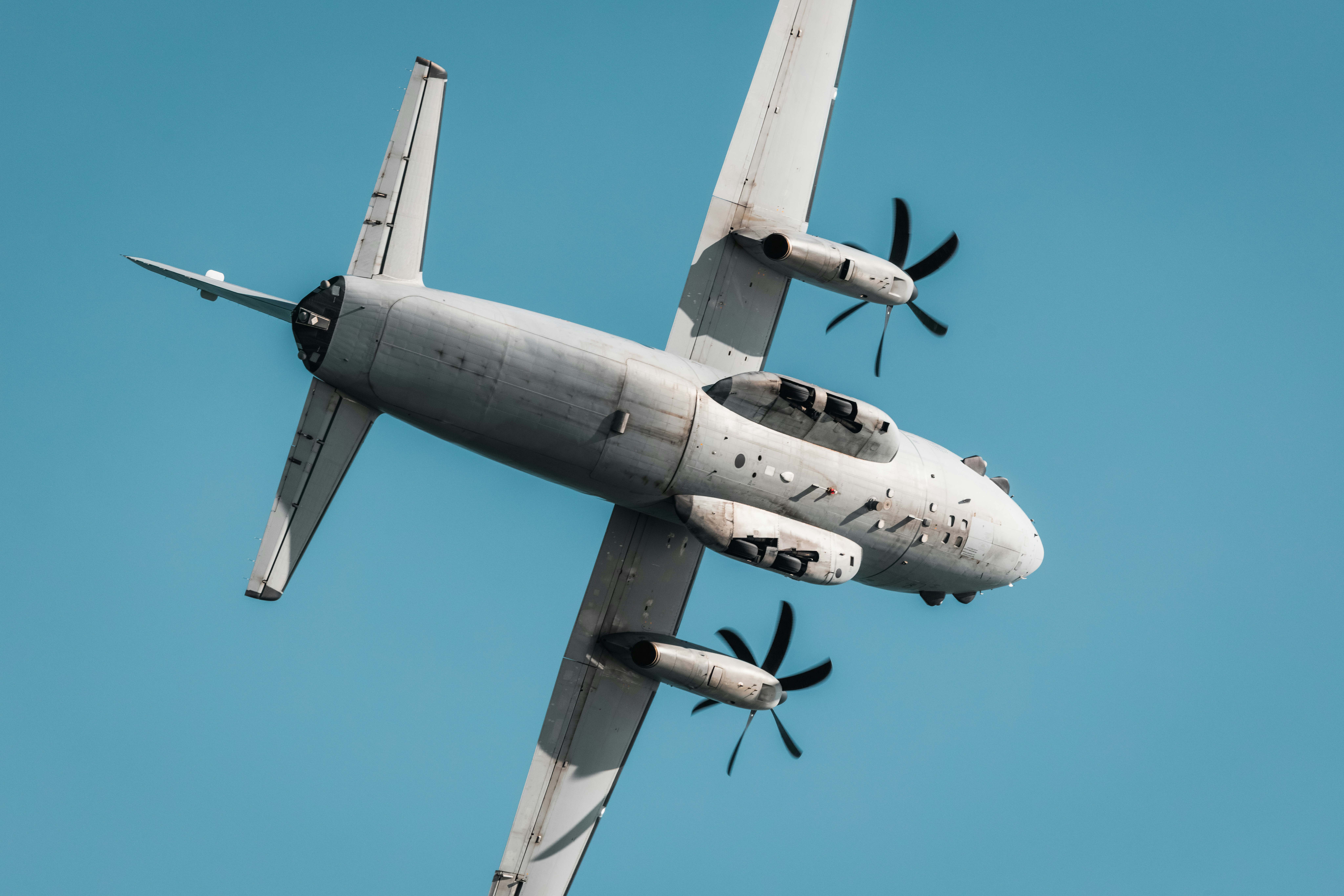 Pesawat turboprop bermesin ganda abu-abu terbang di langit biru cerah
