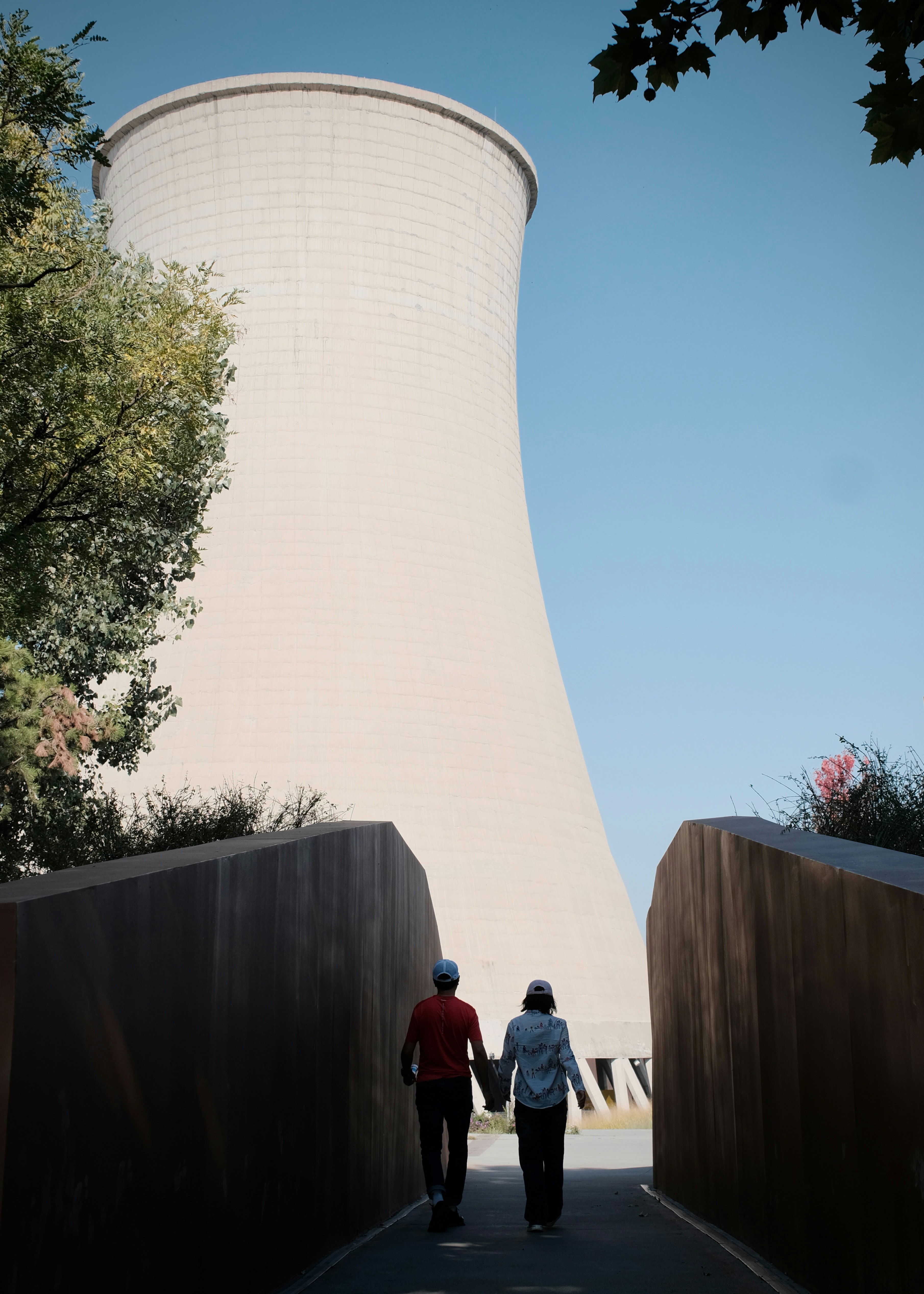 Two people walking on a path toward a large concrete cooling tower