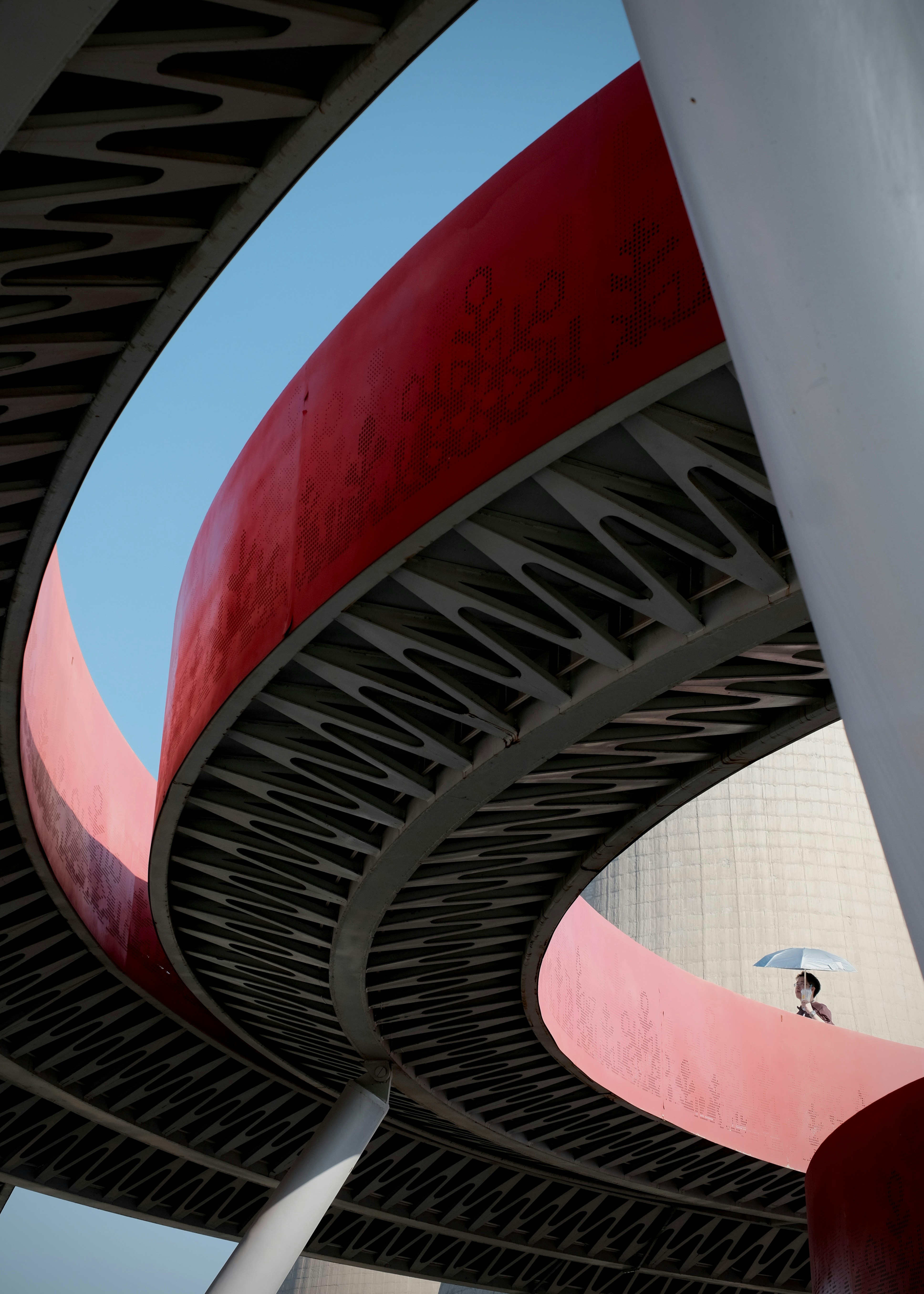 A person with an umbrella walking on a curved red pedestrian bridge