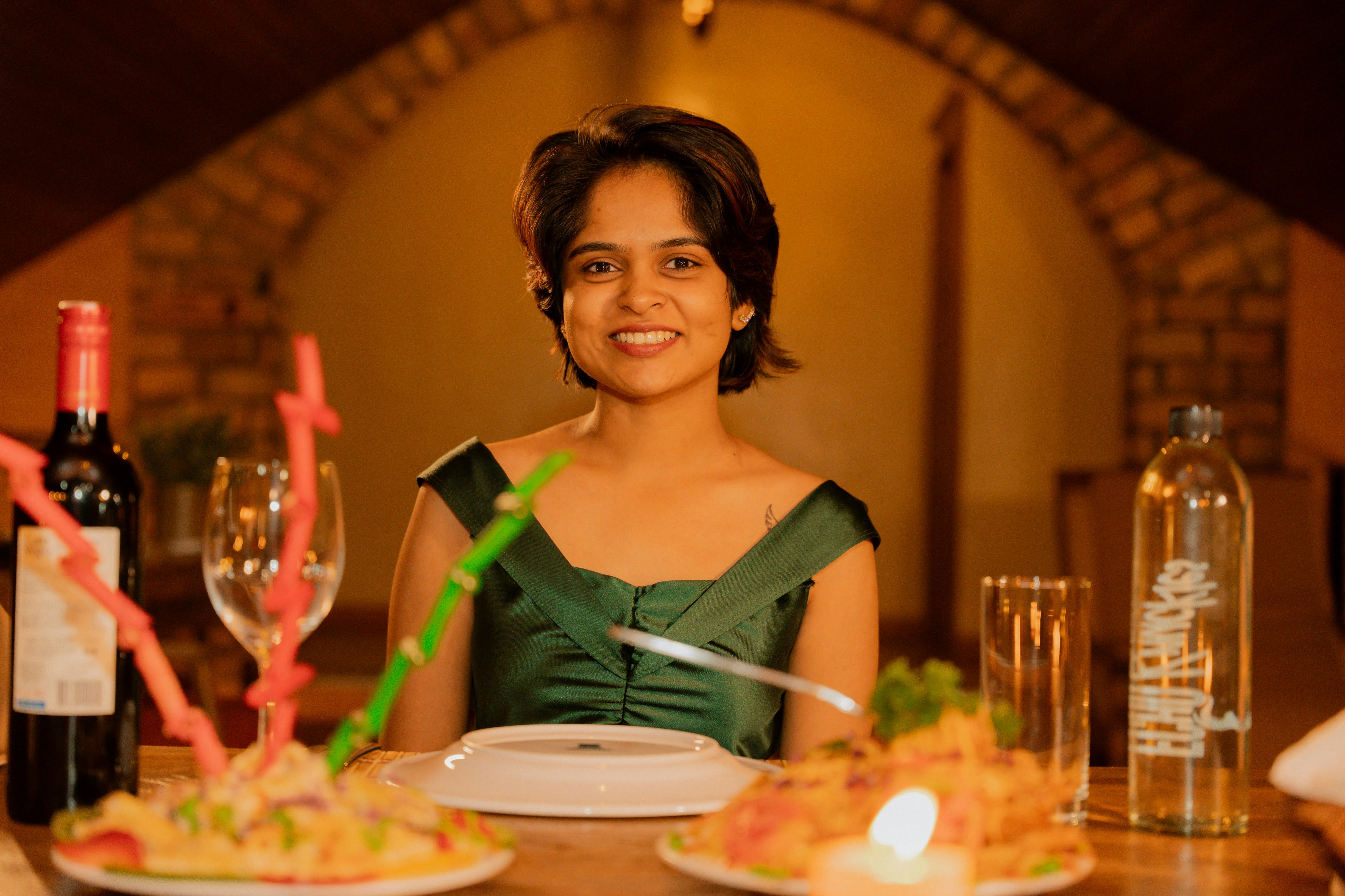 A woman in a green dress sitting at a dinner table with wine and food