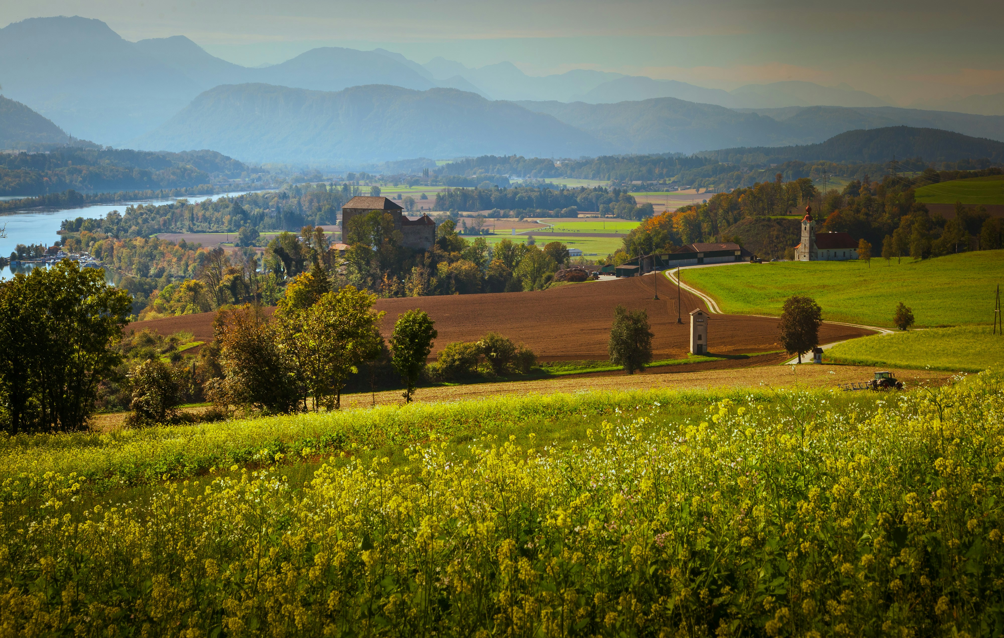 A rural landscape with a castle, a church, and fields under distant mountains