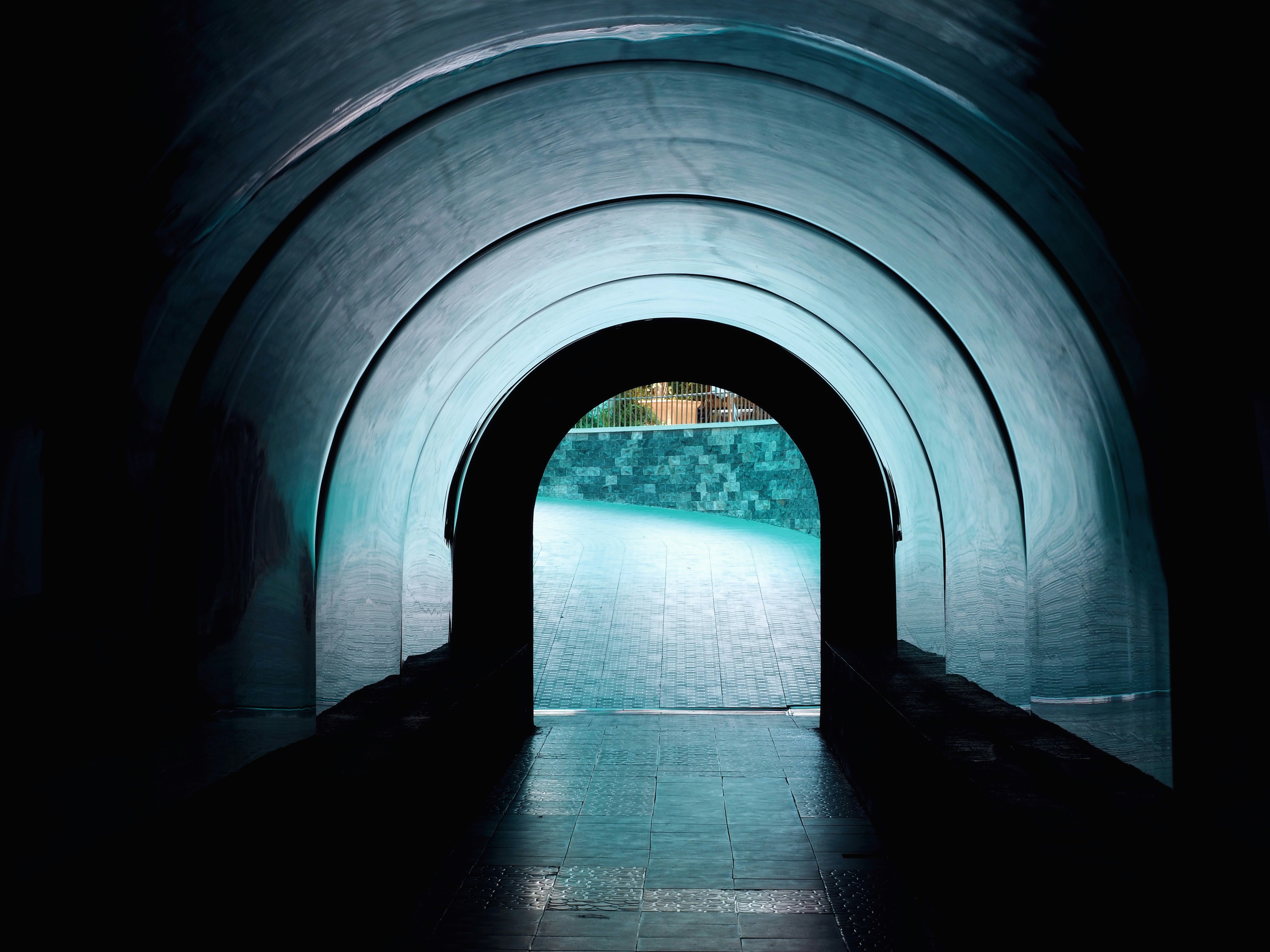 A curved tunnel with blue lighting leading to a bright outdoor paved area