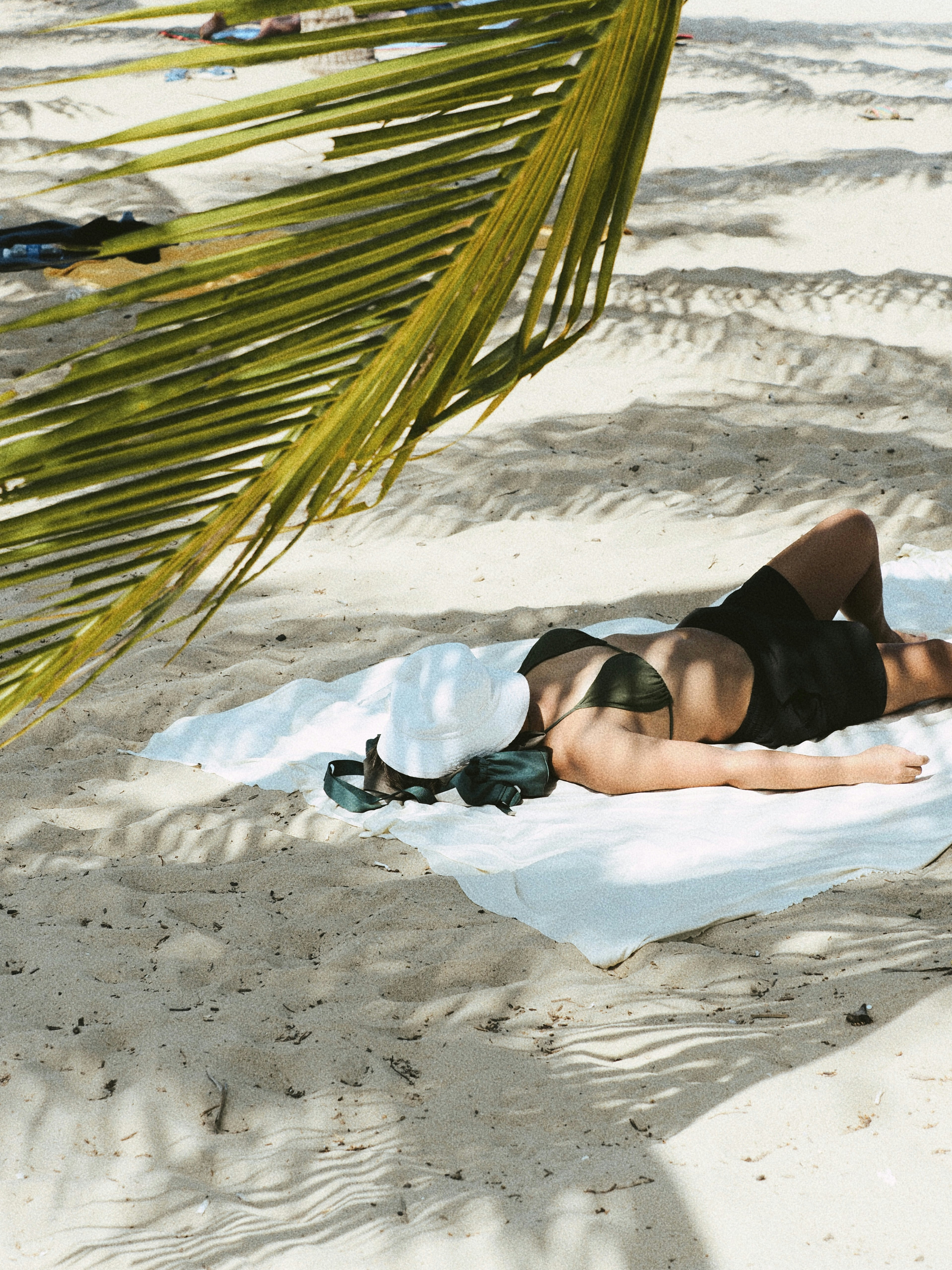 A person in a bikini and white hat lying on a beach towel