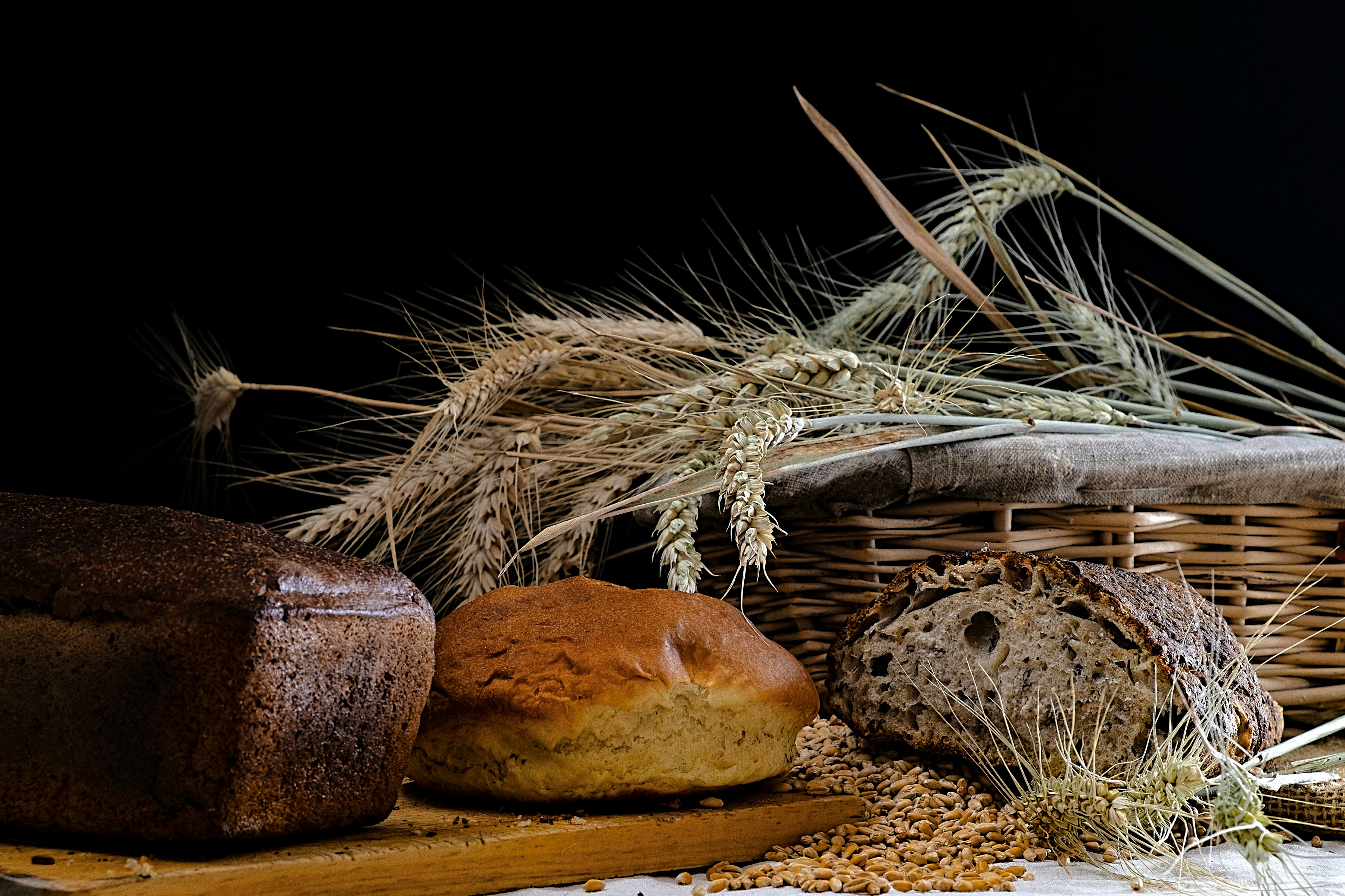 Fotomural Loaves of bread and wheat stalks in a wicker basket on a dark background